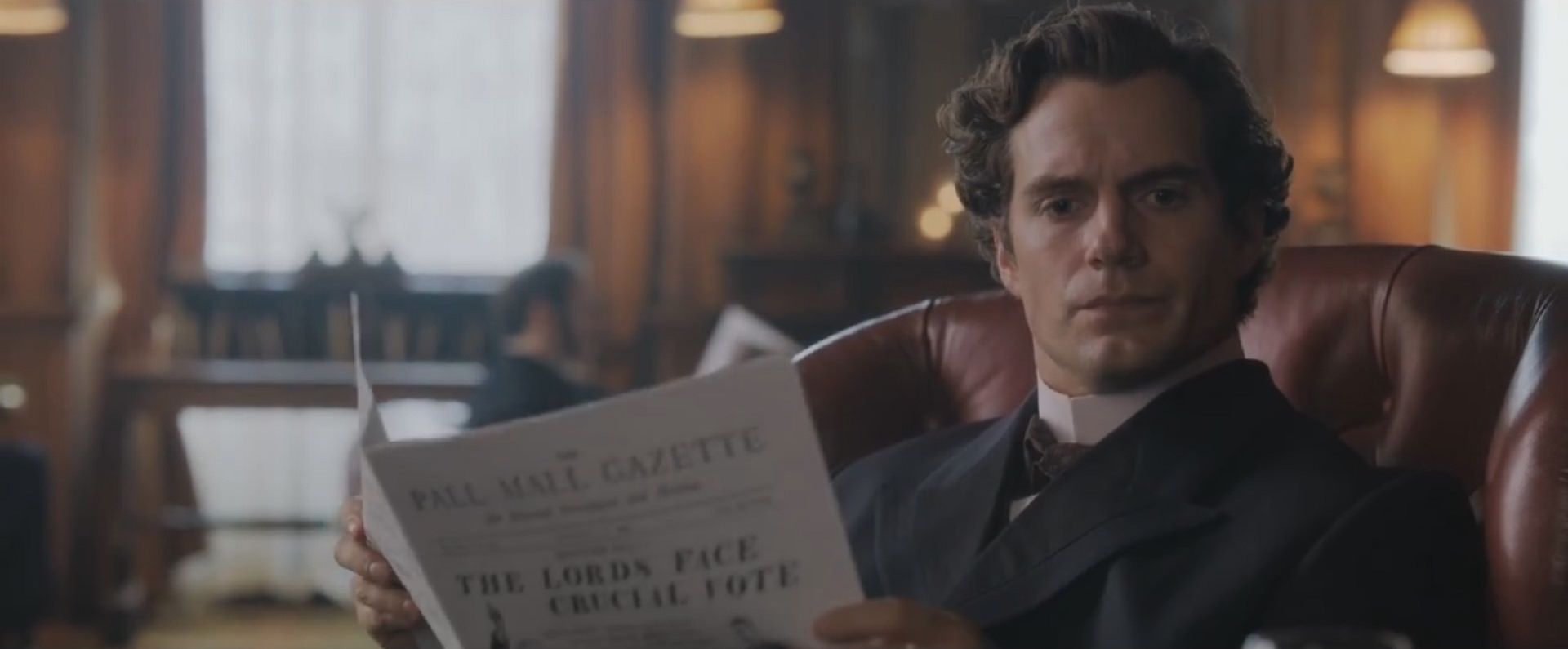 شخصیت شرلوک هولمز با بازی هنری کویل در حال تفکر و در در دست داشتن روزنامه در فیلم Enola Holmes