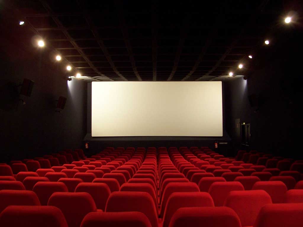 یک سالن خالی سینما با صندلی های قرمز و پرده سفید