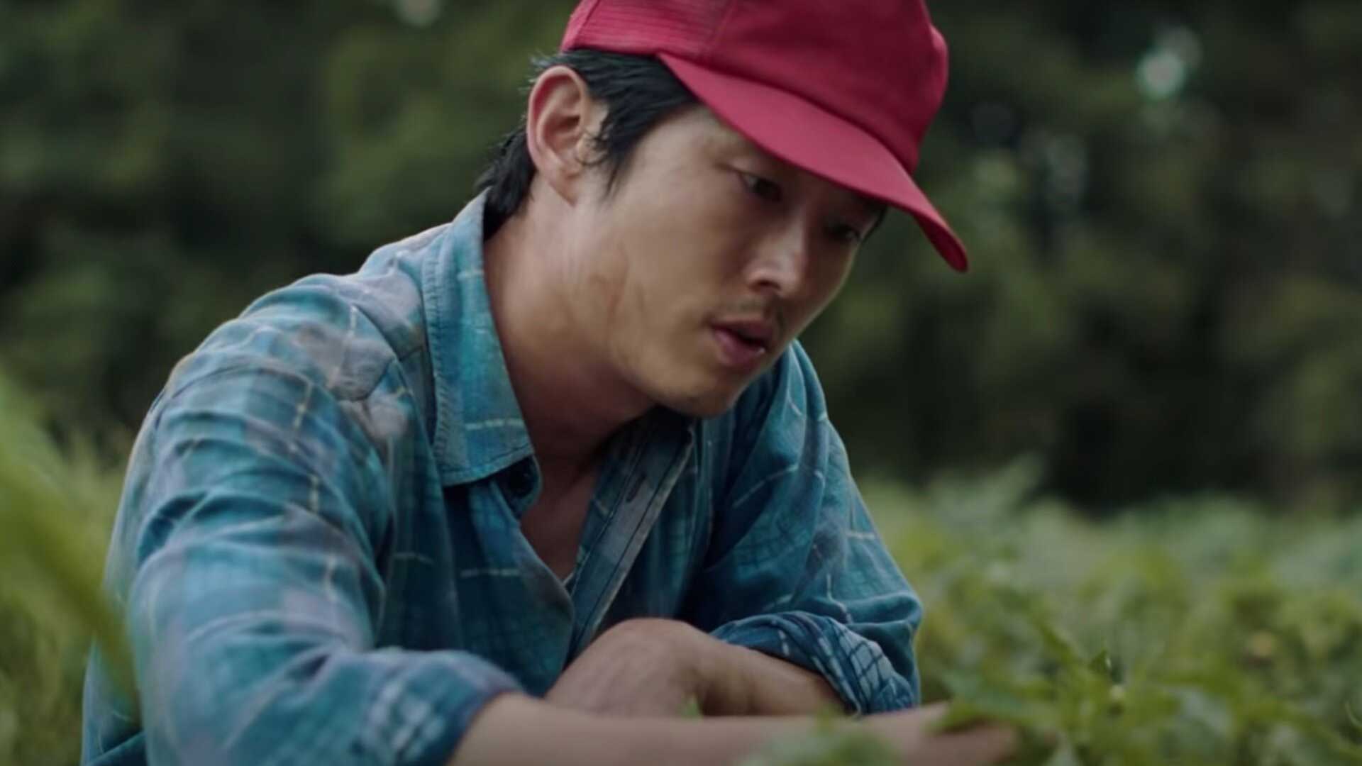 بازیگر کره ای با کلاه قرمز مشغول نگاه انداختن به چمن در فیلم Minari