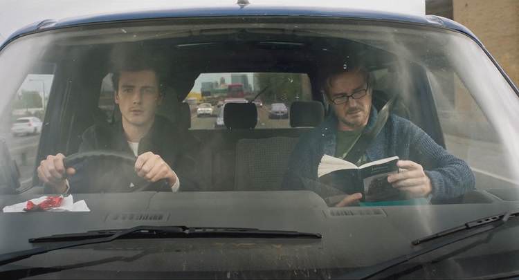 میشائیل ریچاردسون پشت فرمان و لیام نیسون در حال کتاب خواندن در ماشین سیاه رنگ در جاده در فیلم Made in Italy