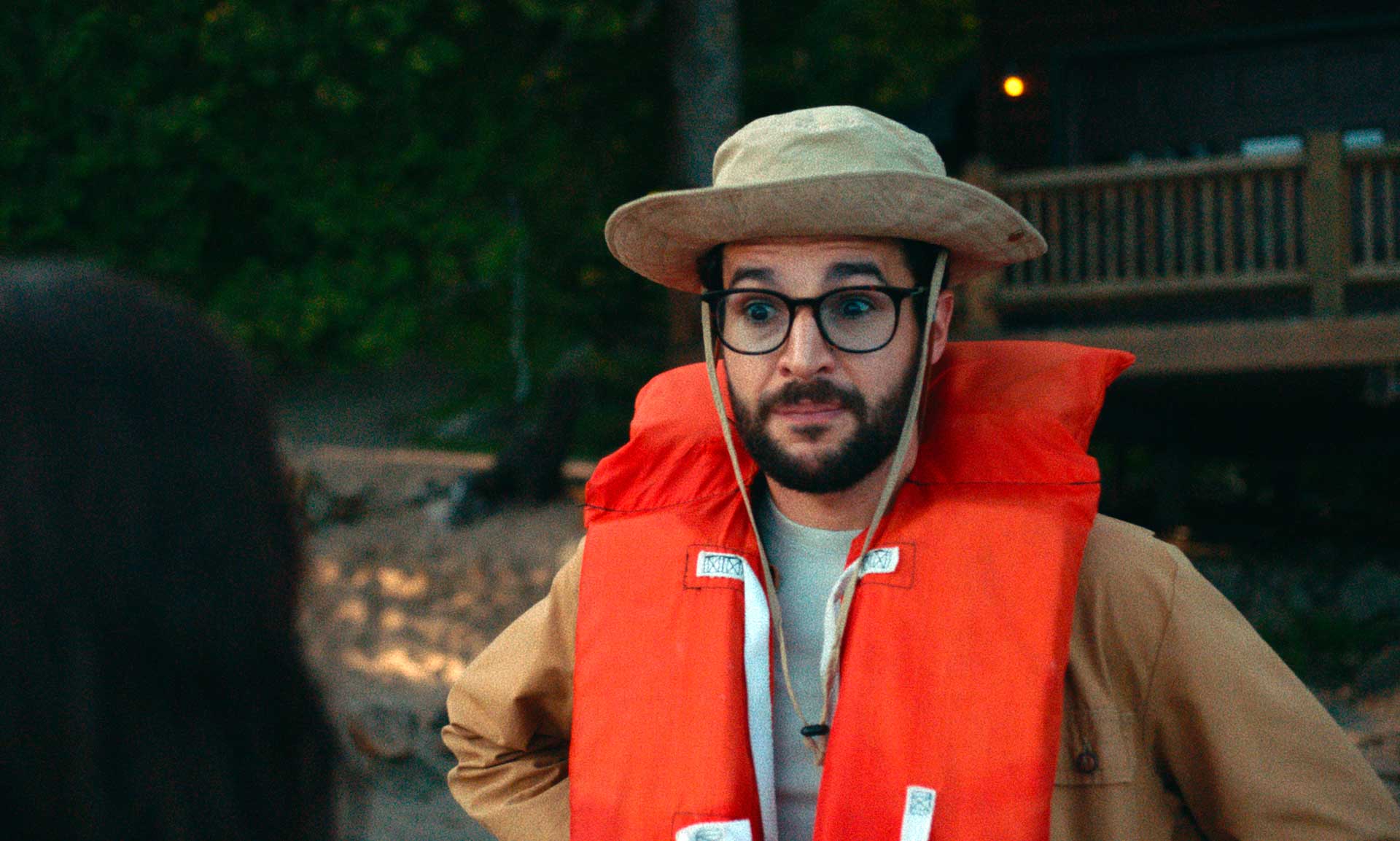 مرد جدی با قیافه مسخره، عینک بزرگ و جلیقه نجات نارنجی رنگ در فضای جنگلی کنار دریاچه فیلم Black Bear