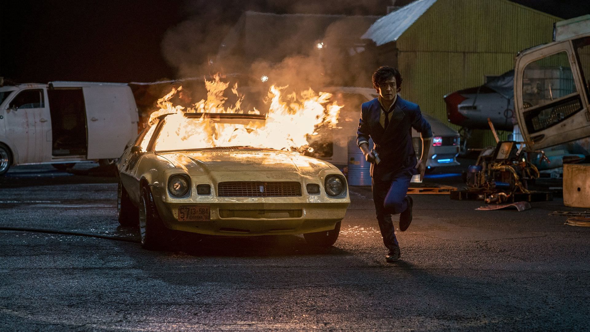 جان چو در نقش اسپایک اسپیگل در حال دویدن درکنار خودرو منفجر شده و در حال سوختن در سریال Cowboy Bebop