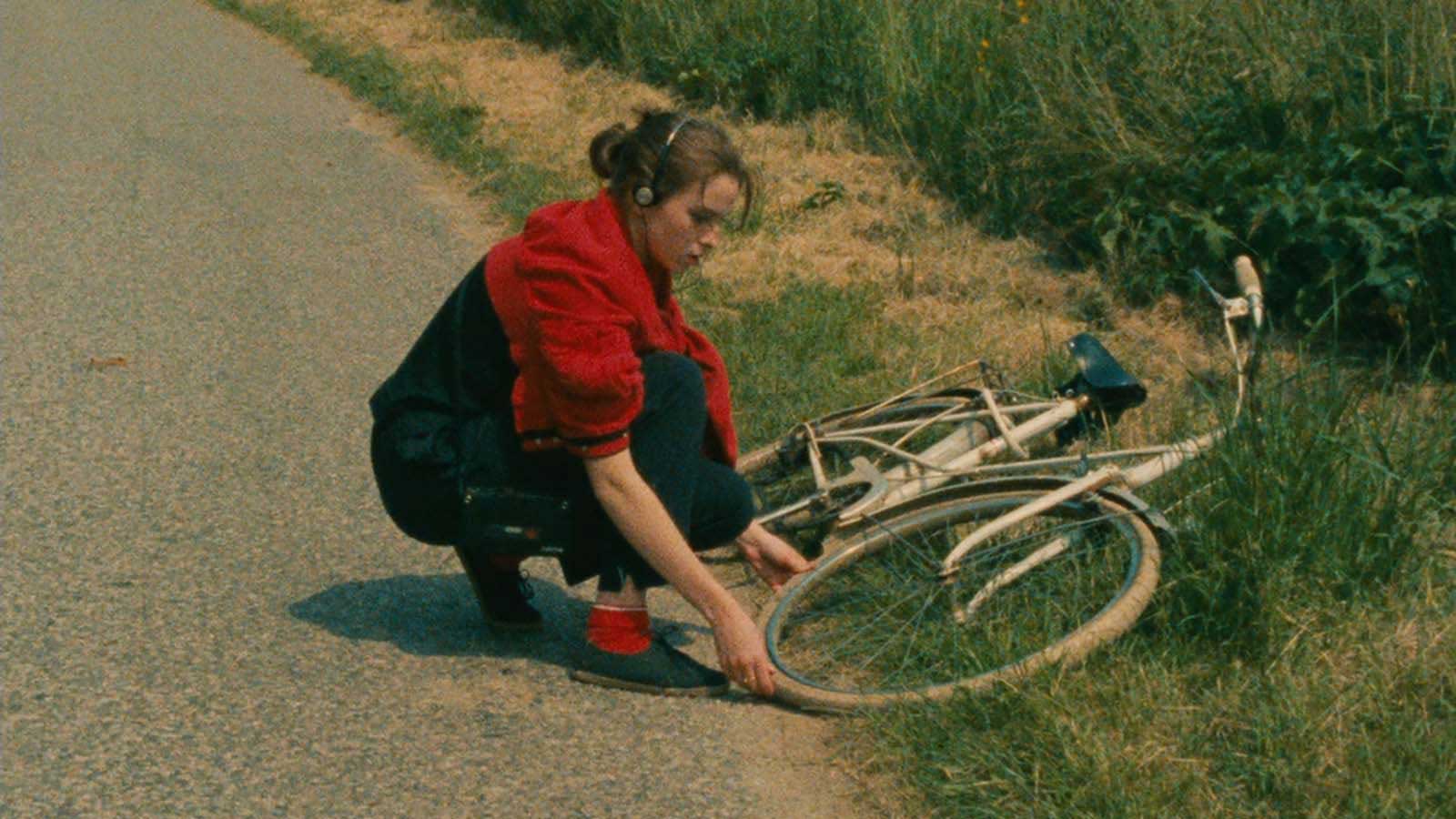 دختر با لباس سرخ کنار جاده با دوچرخه افتاده روی زمین در فیلم Four Adventures of Reinette and Mirabelle