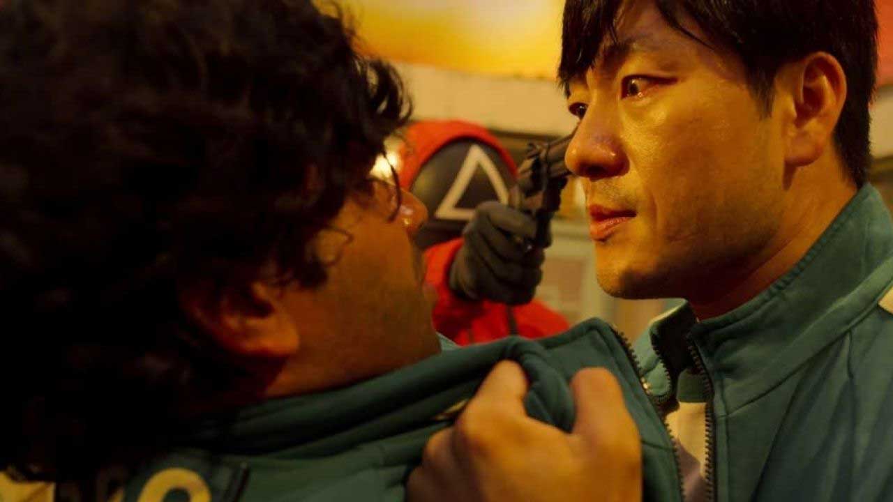 سرباز با لباس صورتی و ماسک دارای علامت مثلث مشغول نشانه گرفتن بازیکن با لباس سبز در سریال کره ای Squid Game نتفلیکس