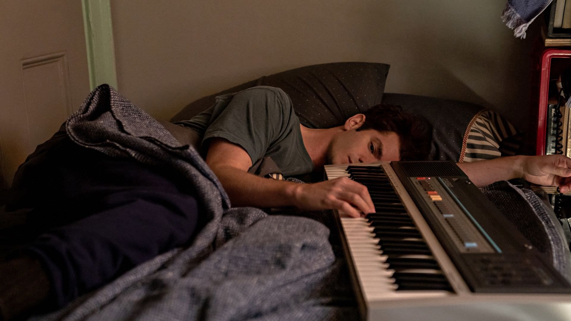 اندرو گارفیلد در نقش جاناتان لارسون در حال زدن پیانو روی تخت در فیلم Tick, Tick... Boom