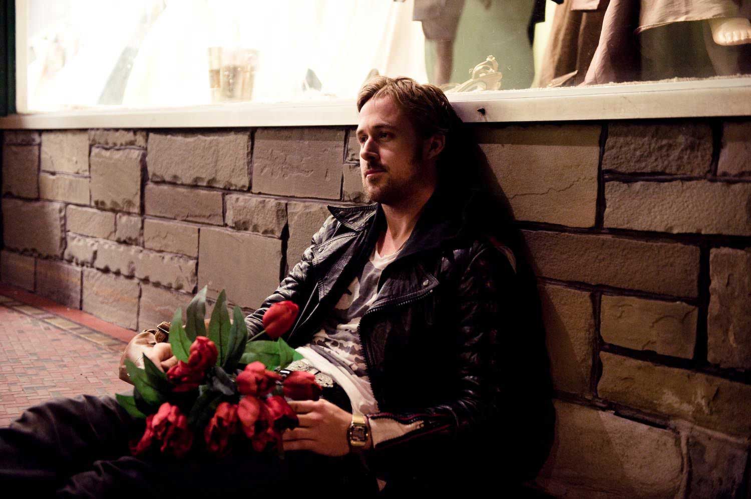 تکیه دادن رایان گاسلینگ جوان به دیوار در حال نگه داشتن گل های قرمز در فیلم Blue Valentine