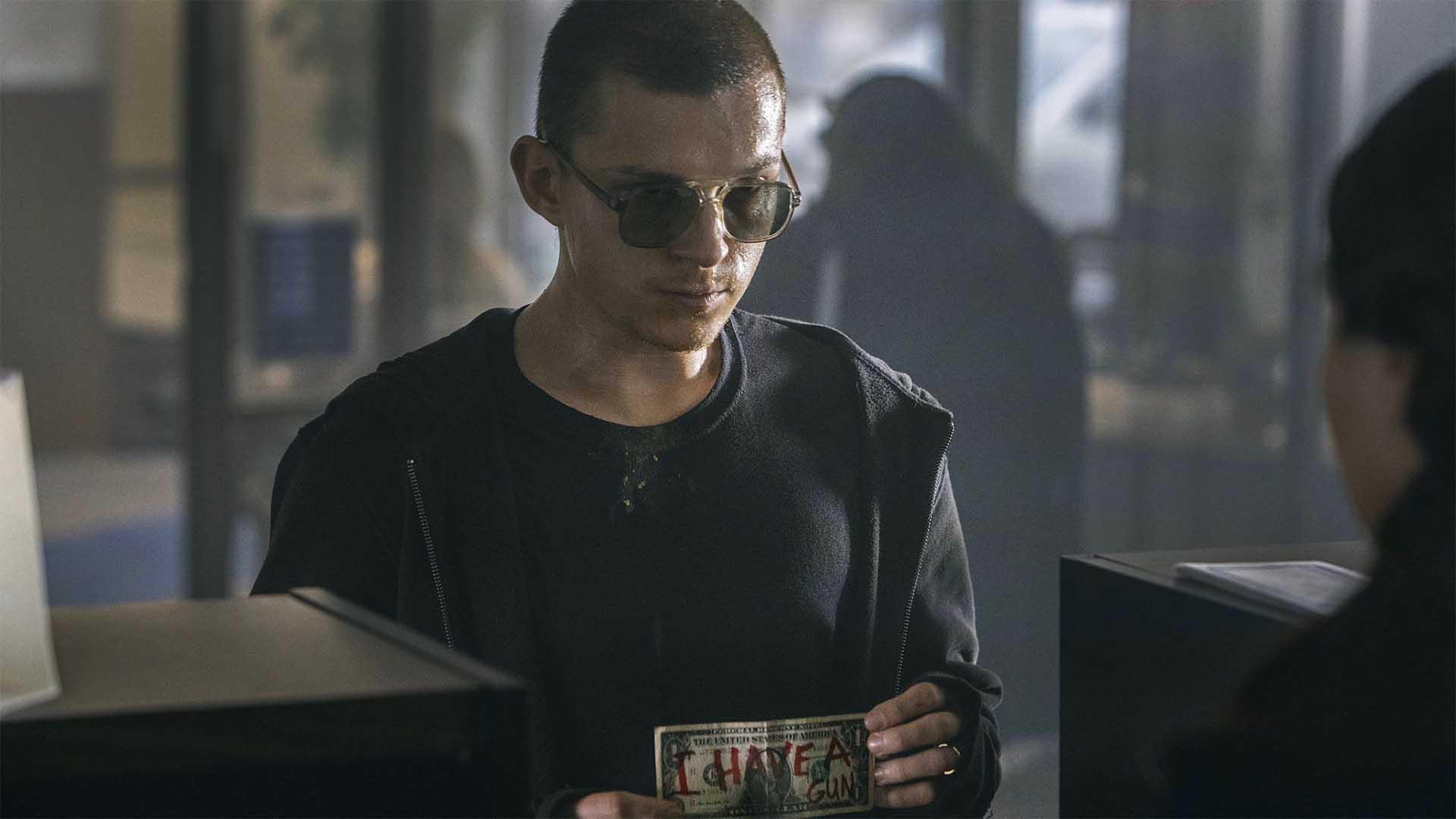 تام هالند به همراه عینک دودی در فیلم Cherry یک اسکناس دلار در دست دارد