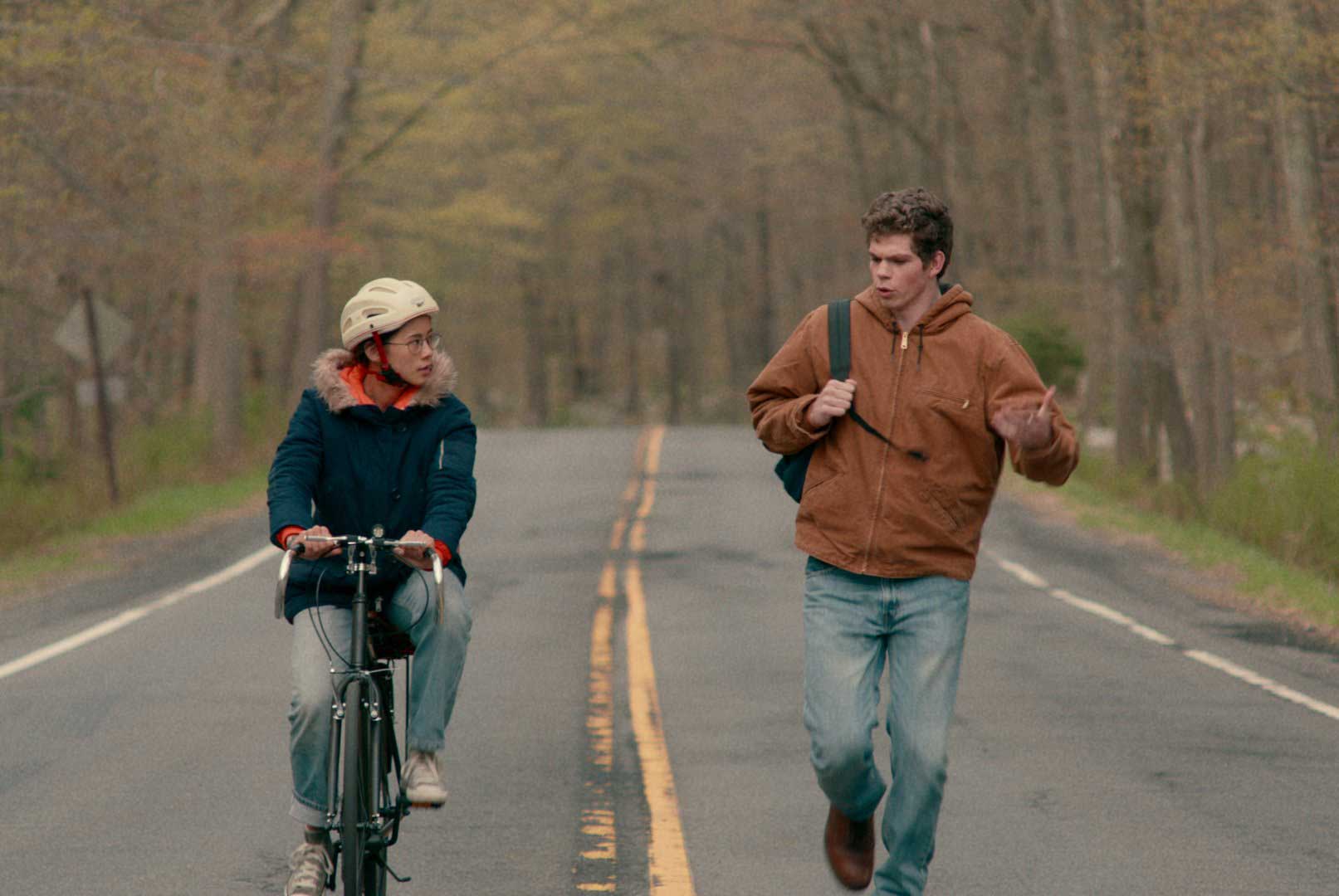 فیلم The Half of It صحبت دو دوست در میان خیابان واقع احاطه شده با درختان در حال دوچرخه سواری و پیاده روی