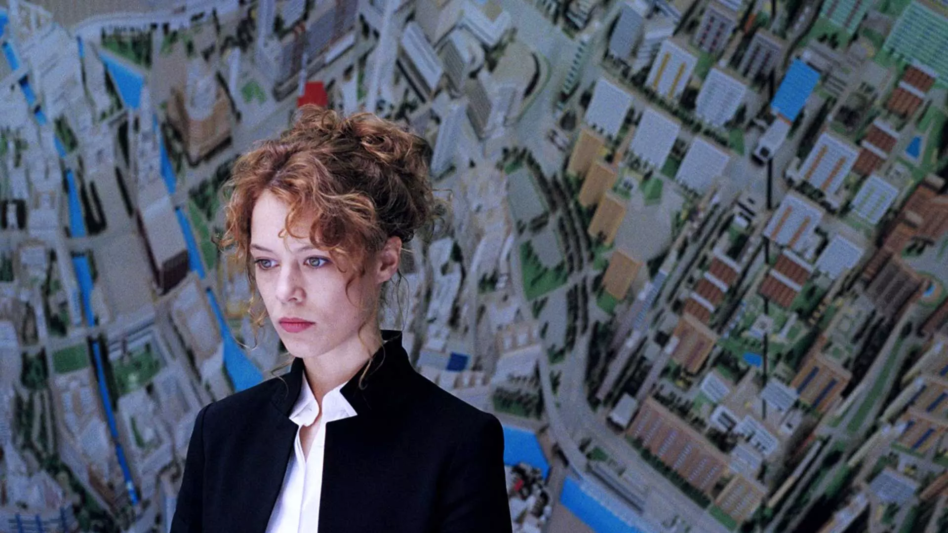 سر رو به پایین زن با کت سیاه و موهای قرمز مقابل نقشه شهر در فیلم رمانتیک Undine