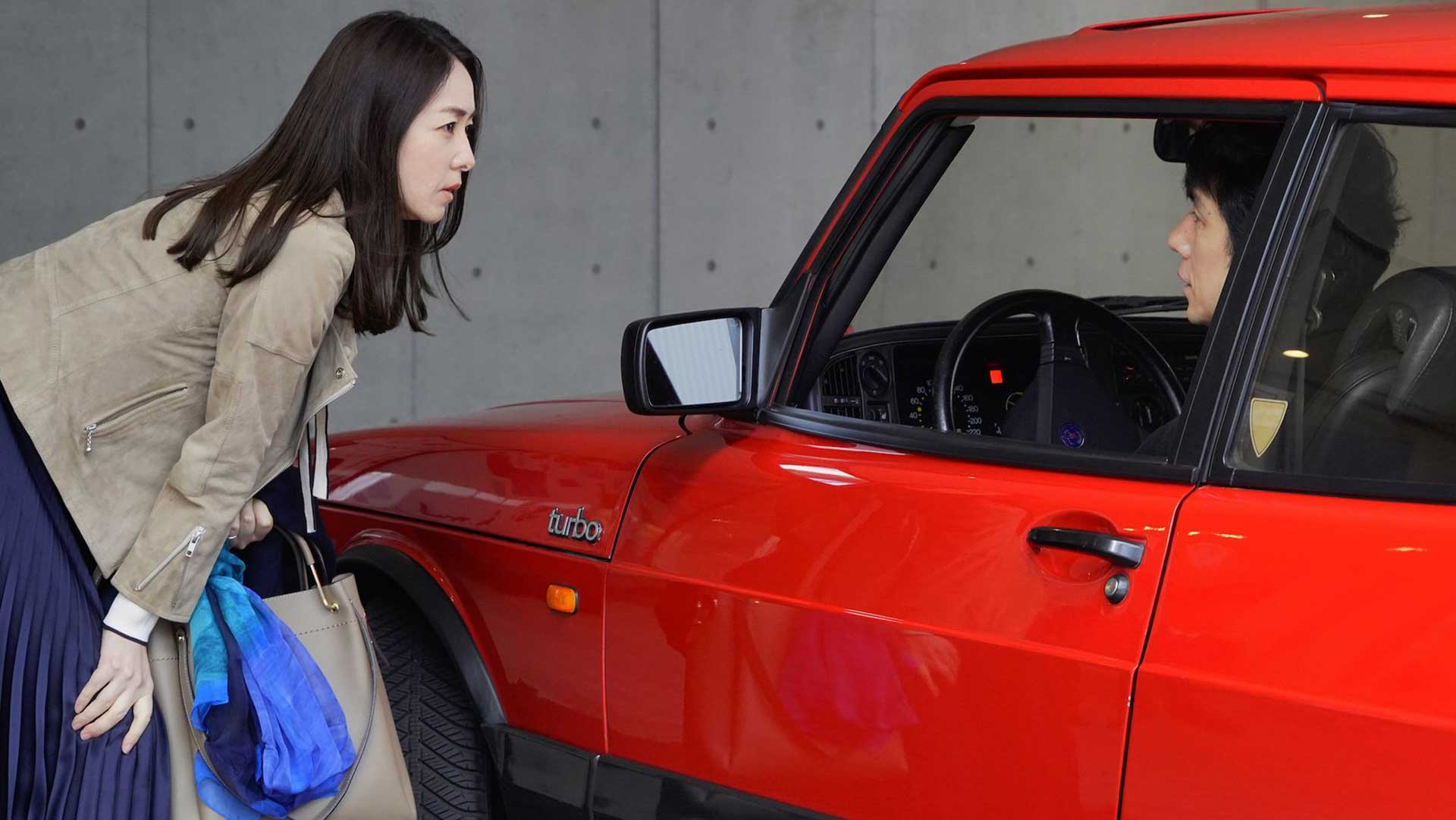 دختر آسیایی در حال نگاه به راننده ماشین قرمزرنگ در فیلم Drive My Car ریوسوکی هاماگوچی، برنده جایزه بهترین فیلمنامه جشنواره کن و حاضر در جشنواره تورنتو