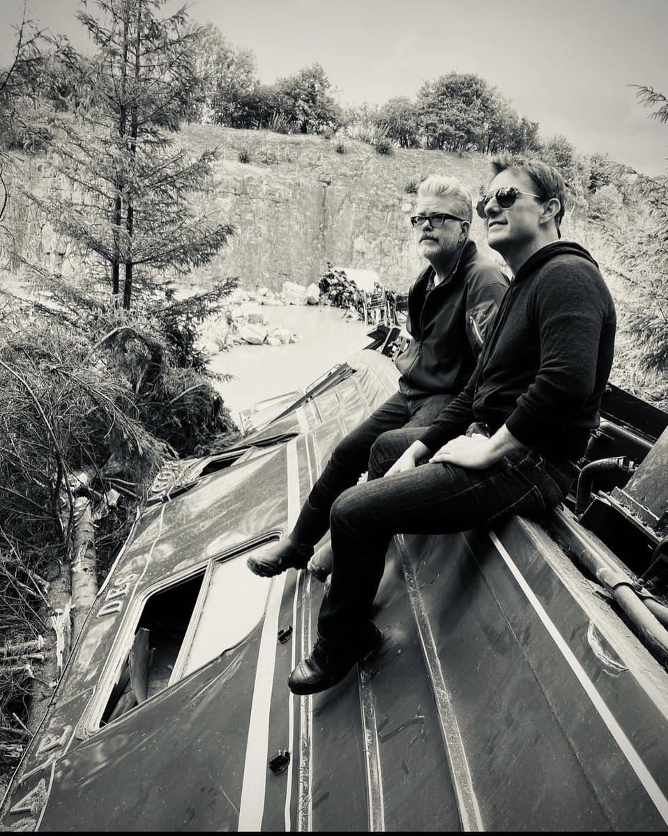 تام کروز و کریستوفر مک کوری درکنار هم روی قطار سقوط کرده در پشت صحنه فیلمبرداری فیلم Mission Impossible 7 نشسته‌اند