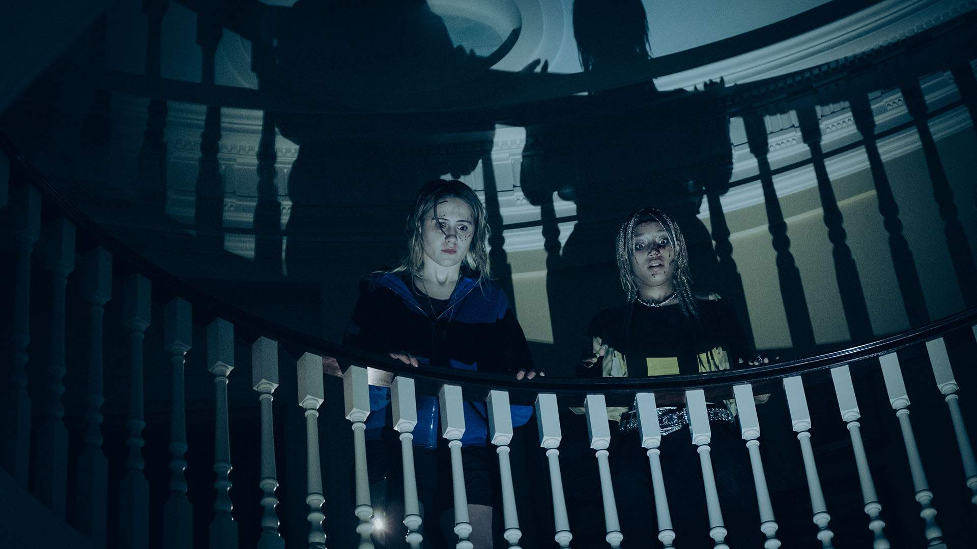 ماریا باکالوا و آماندلا استنبرگ در فیلم Bodies Bodies Bodies به جسد دوستشان در پایین پله‌ها نگاه می‌کنند