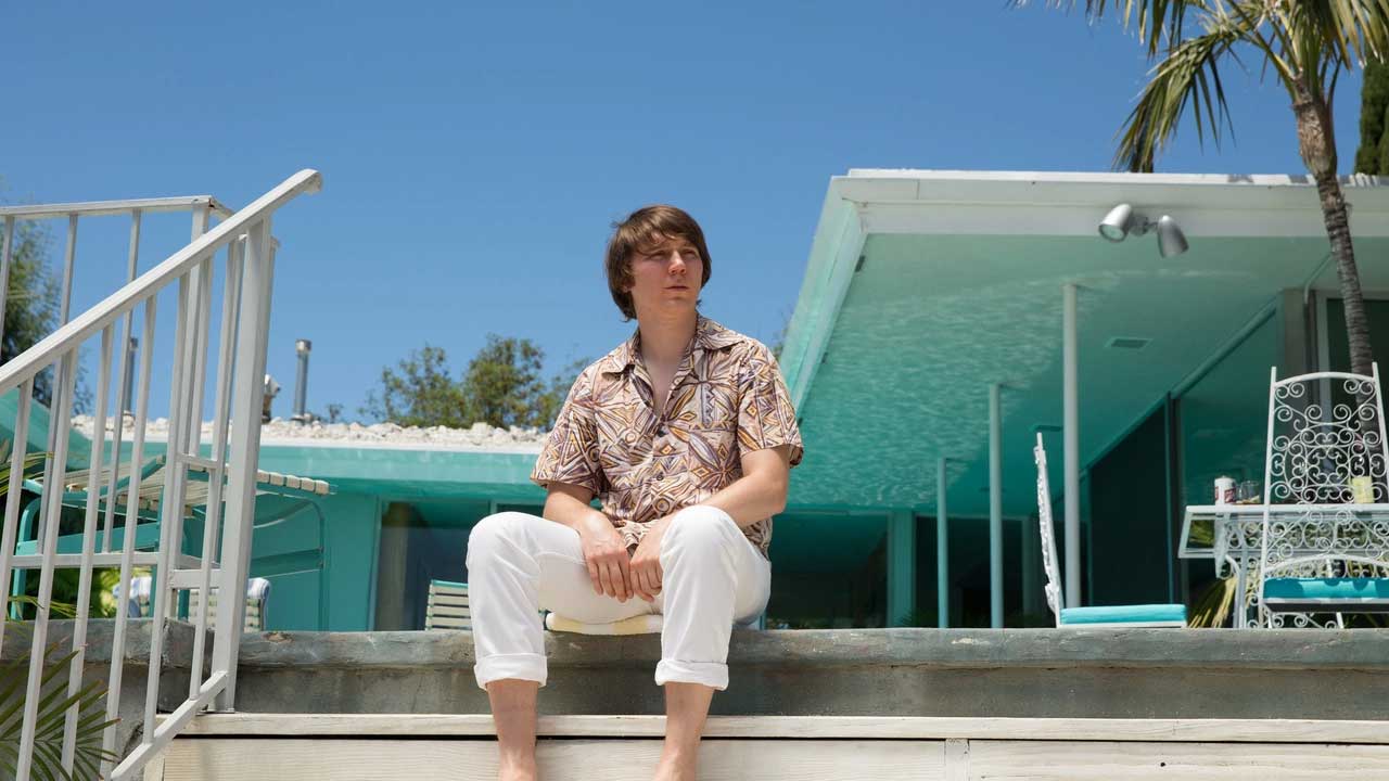 پل دینو با پیراهن آستین کوتاه و شلوار سفید روی پله ها در فیلم Love & Mercy، محصول سال ۲۰۱۴ میلادی