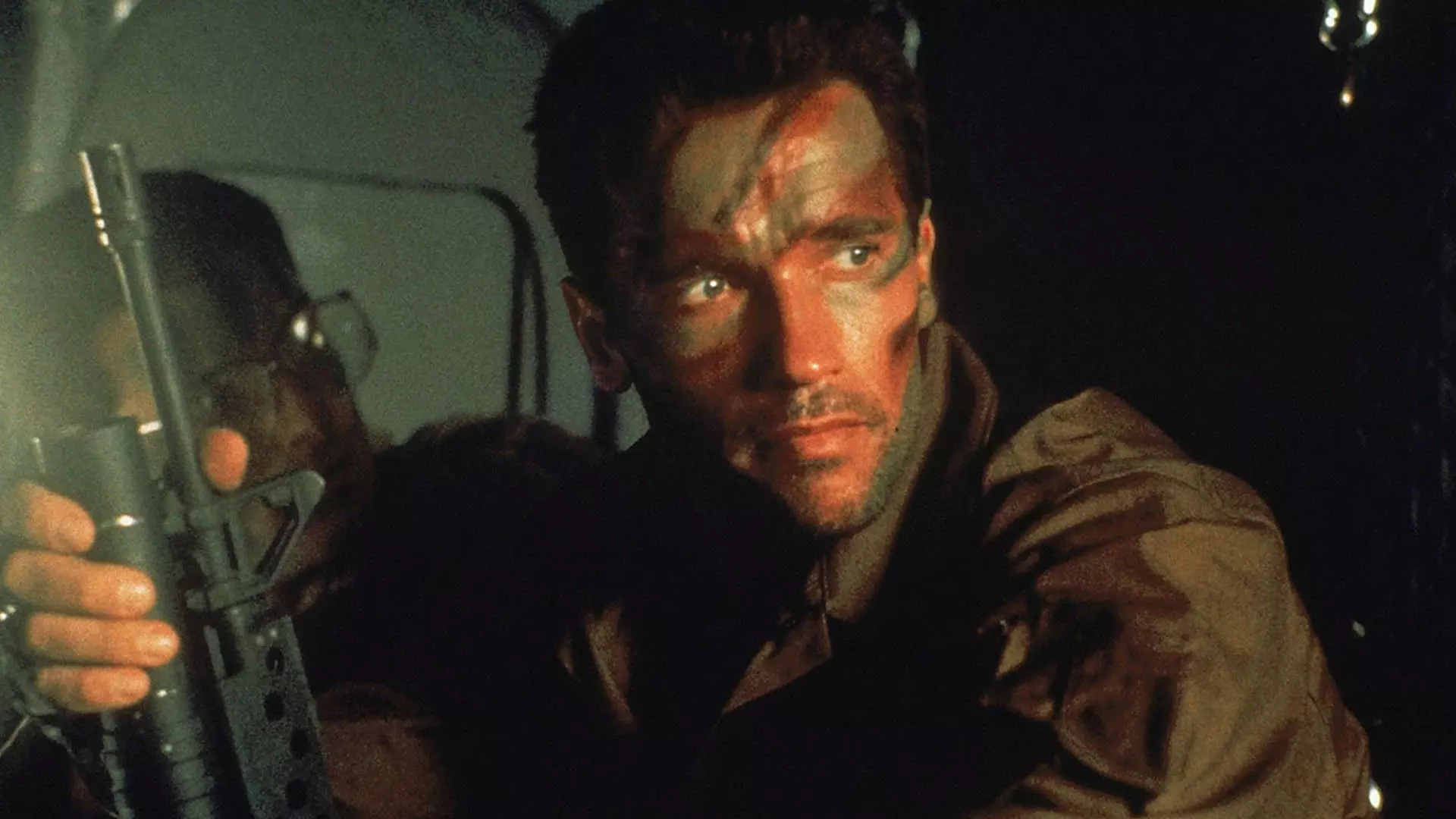 آرنولد شوارتزنگر با اسلحه و صورتی رنگ شده در فیلم Predator