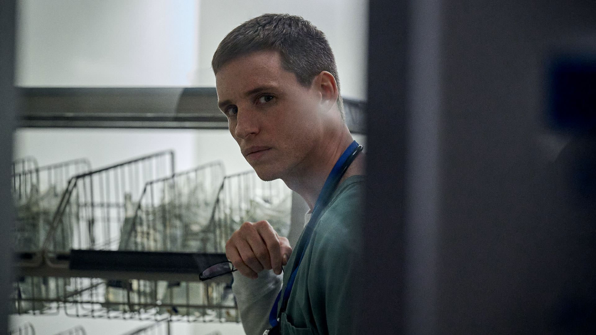 Eddie Redmayne portant un uniforme d'infirmière dans un entrepôt d'hôpital dans une scène du film The Good Nurse réalisé par Tobias Lindholm.