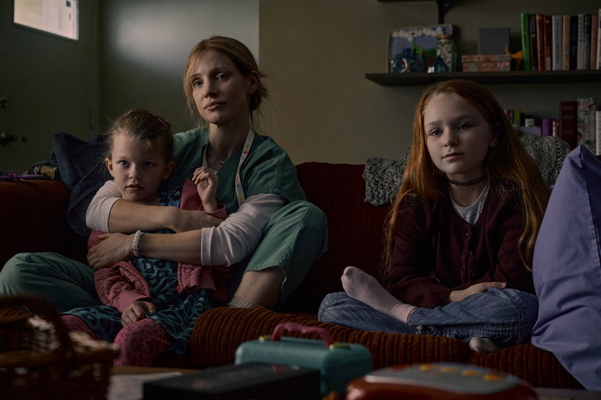Jessica Chastain tenant un garçon assis à côté d'une petite fille sur un canapé dans une maison dans une scène du film Good Nurse réalisé par Tobias Lindholm.