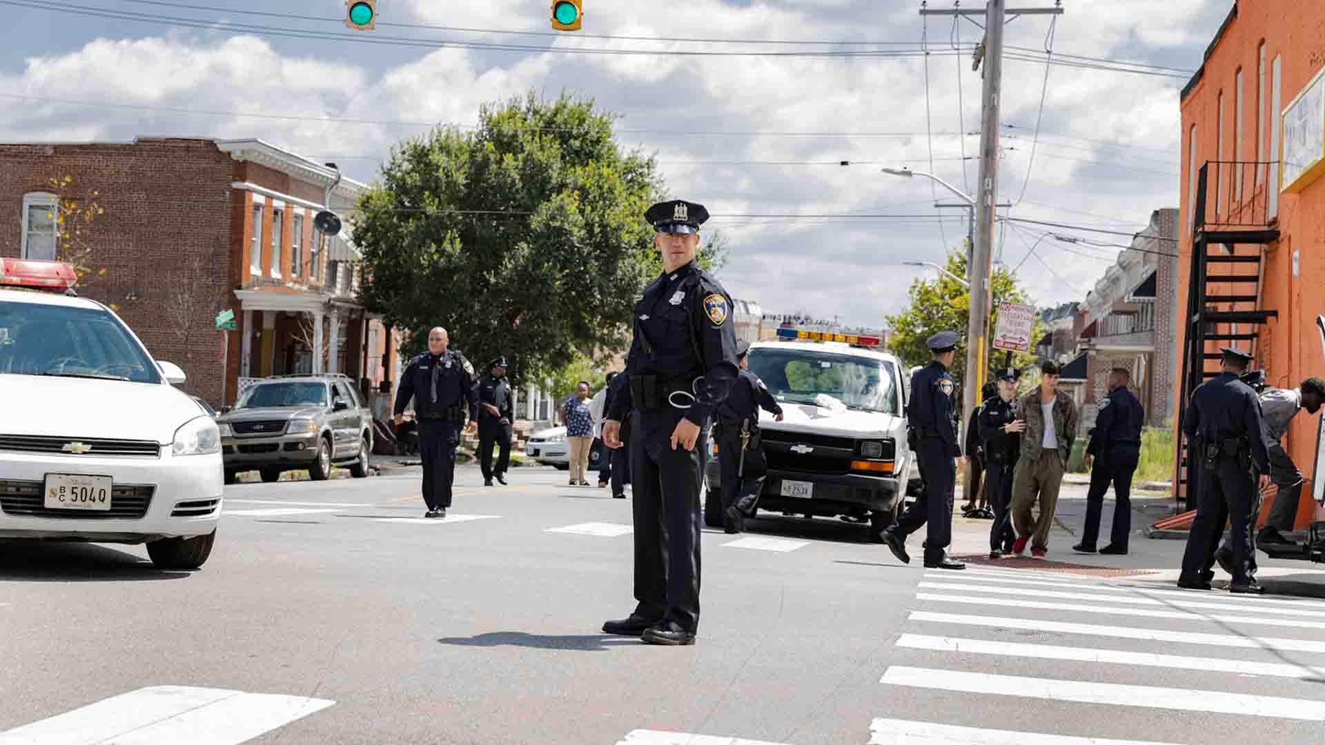 جان برنتال با لباس پلیس در سریال We Own This City وسط خیابان ایستاده است