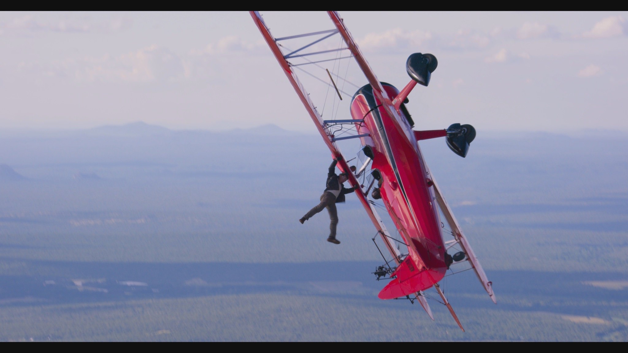 تام کروز در نقش ایتن هانت در پشت صحنه فیلمبرداری فیلم Mission: Impossible – Dead Reckoning Part Two از یک هواپیمای قدیمی قرمز رنگ آویزان شده است