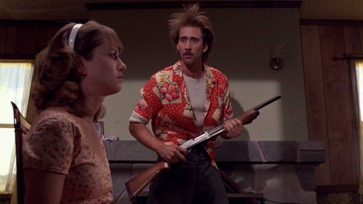 نیکلاس کیج با تفنگ بزرگ در حال صحبت با همسر خود در فیلم کمدی سیاه Raising Arizona به کارگردانی برادران کوئن