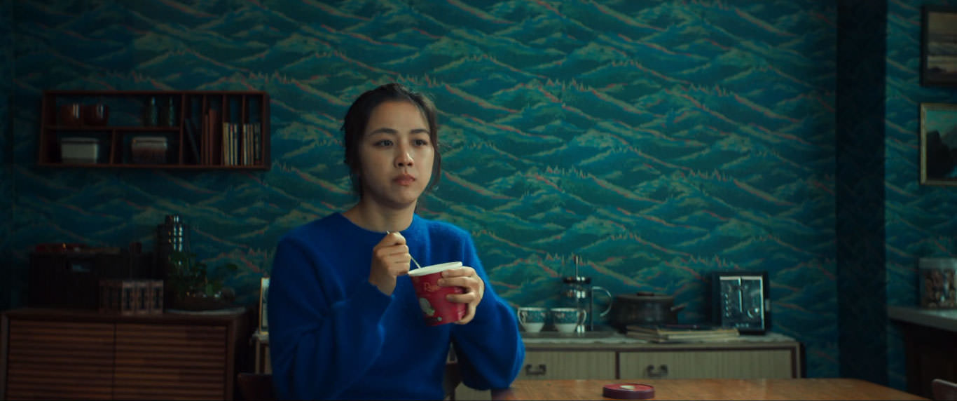 تانگ وی در حال بستنی خوردن پشت به دیواری منقش به تصاویر کوه و آب در نمایی از فیلم عزم رفتن به کارگردانی پارک چان ووک