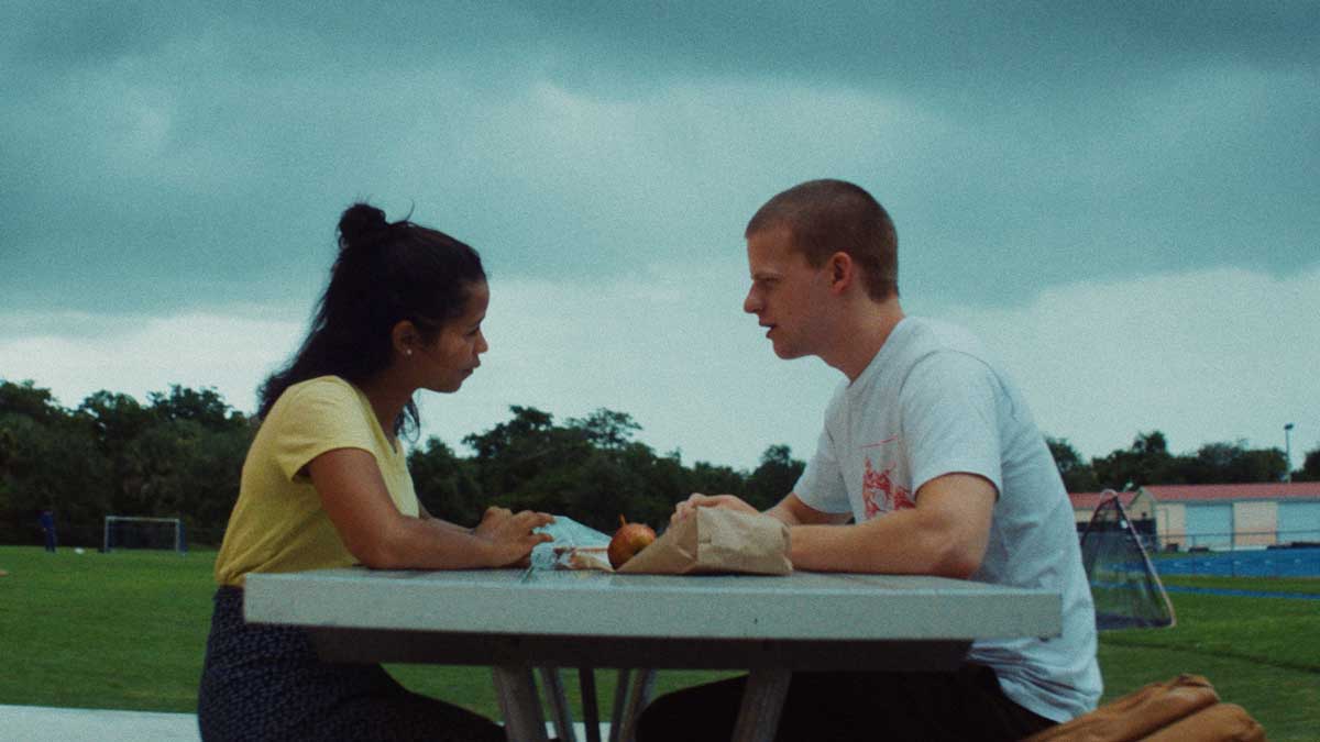 گفت و گو پسر با تی شرت و دختر با لباس زرد سر میز مقابل زمین چمن در فیلم Waves، محصول سال ۲۰۱۹ میلادی