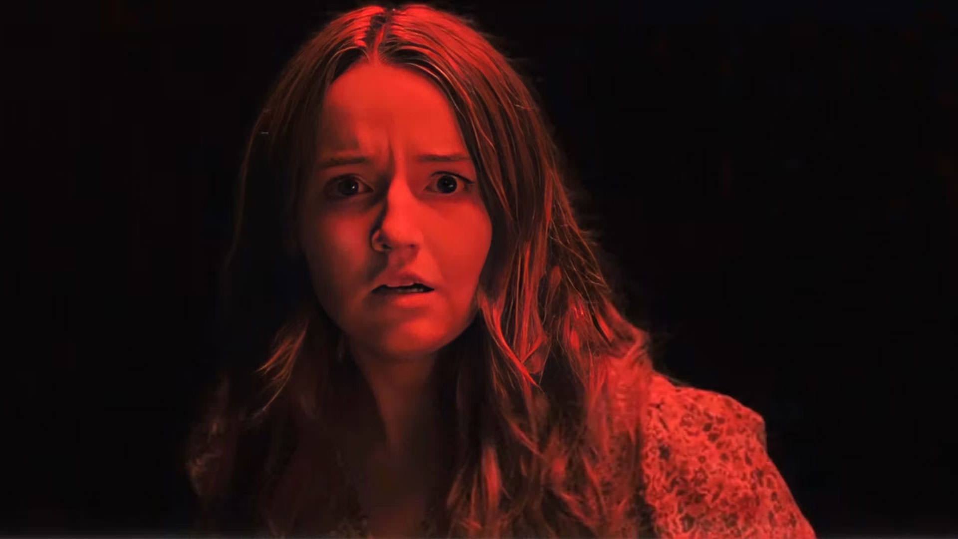 کیتلین دیور که نوری قرمز بر او تابیده است با چهره‌ای متعجب در نمایی از فیلم هیچ‌کس نجاتت نخواهد داد به کارگردانی برایان دافیلد