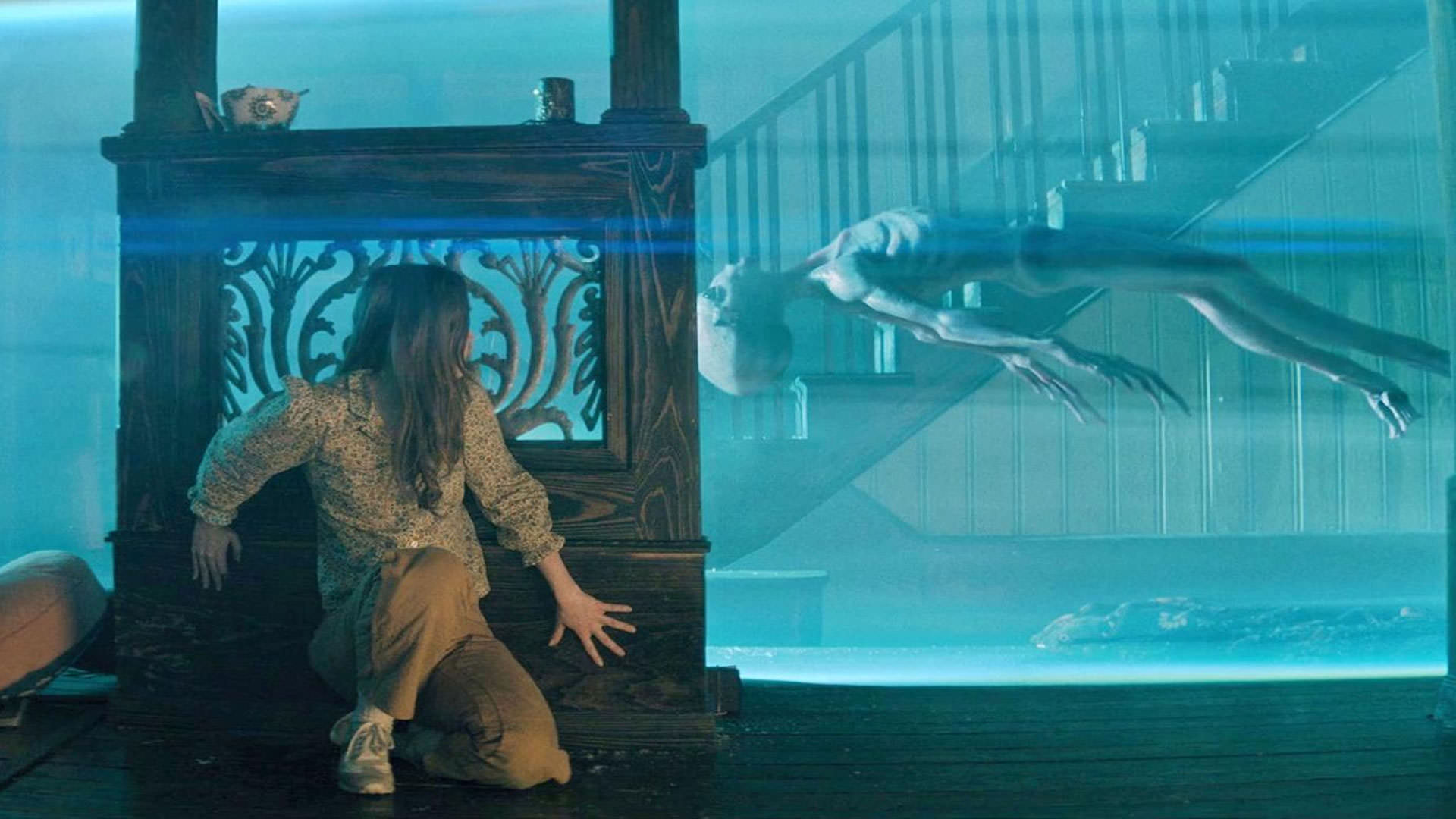 کیتلین دیور پشت یک ستون چوبی پناه گرفته است در حالی که یک بیگانه‌ی خاکستری در میان نوری آبی رنگ میان زمین و هوا معلق است در نمایی از فیلم هیچ‌کس نجاتت نخواهد داد به کارگردانی برایان دافیلد