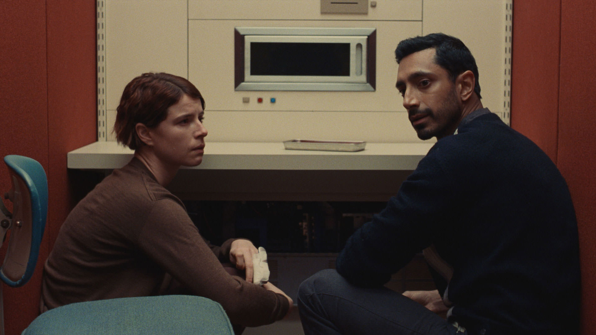 Riz Ahmed assis à côté de Jesse Buckley devant une machine dans une scène du film Nail réalisé par Christos Nico