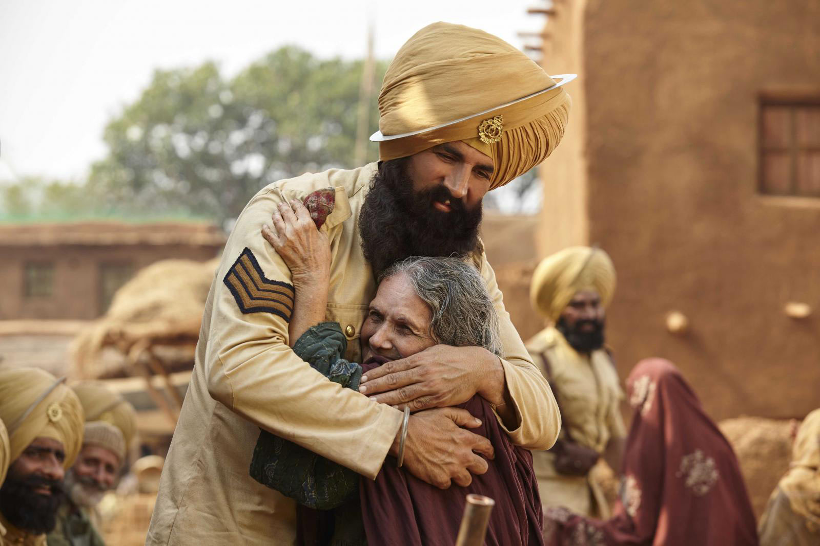 آکشی کومار در نقش سرباز سیک ارتش هند در فیلم زعفرانی درحالی که پیرزنی را در آغوش گرفته است