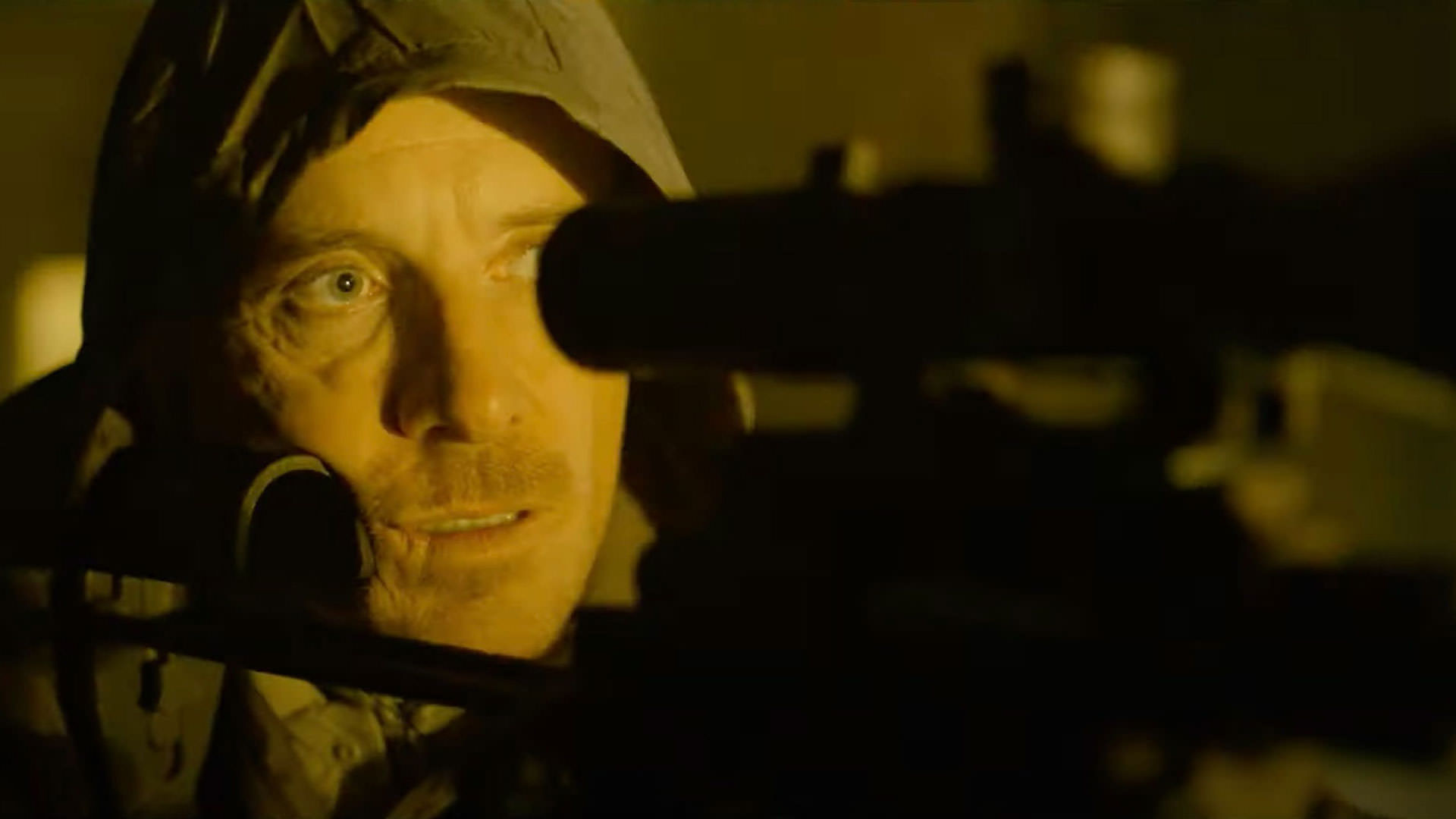 مایکل فاسبندر در حال نشانه‌گیری یک تفنگ تک‌تیر‌انداز در حالی که نوری زردرنگ بر صورت‌اش تابیده است در نمایی از فیلم قاتل به کارگردانی دیوید فینچر