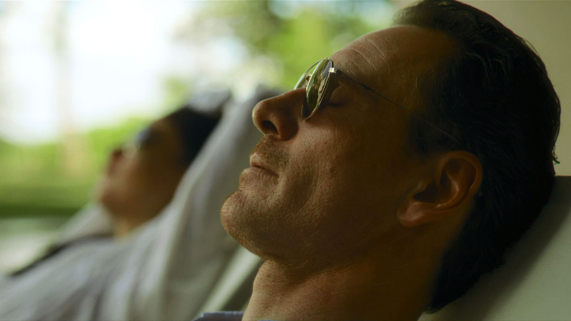 مایکل فاسبندر دراز کشیده با چشمانی بسته و عینک آفتابی بر چشم در نمایی از فیلم قاتل به کارگردانی دیوید فینچر
