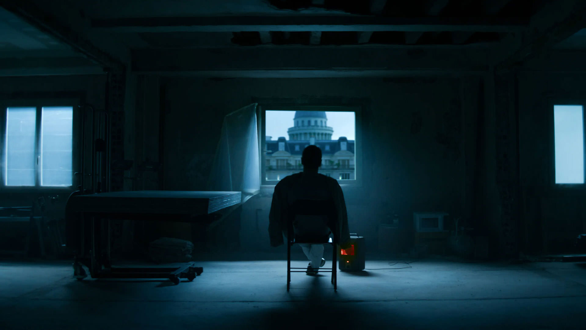 مایکل فاسبندر نشسته روی یک صندلی وسط یک اتاق خالی و تاریک روبه‌روی یک پنجره‌ی کوچک در نمایی از فیلم قاتل به کارگردانی دیوید فینچر