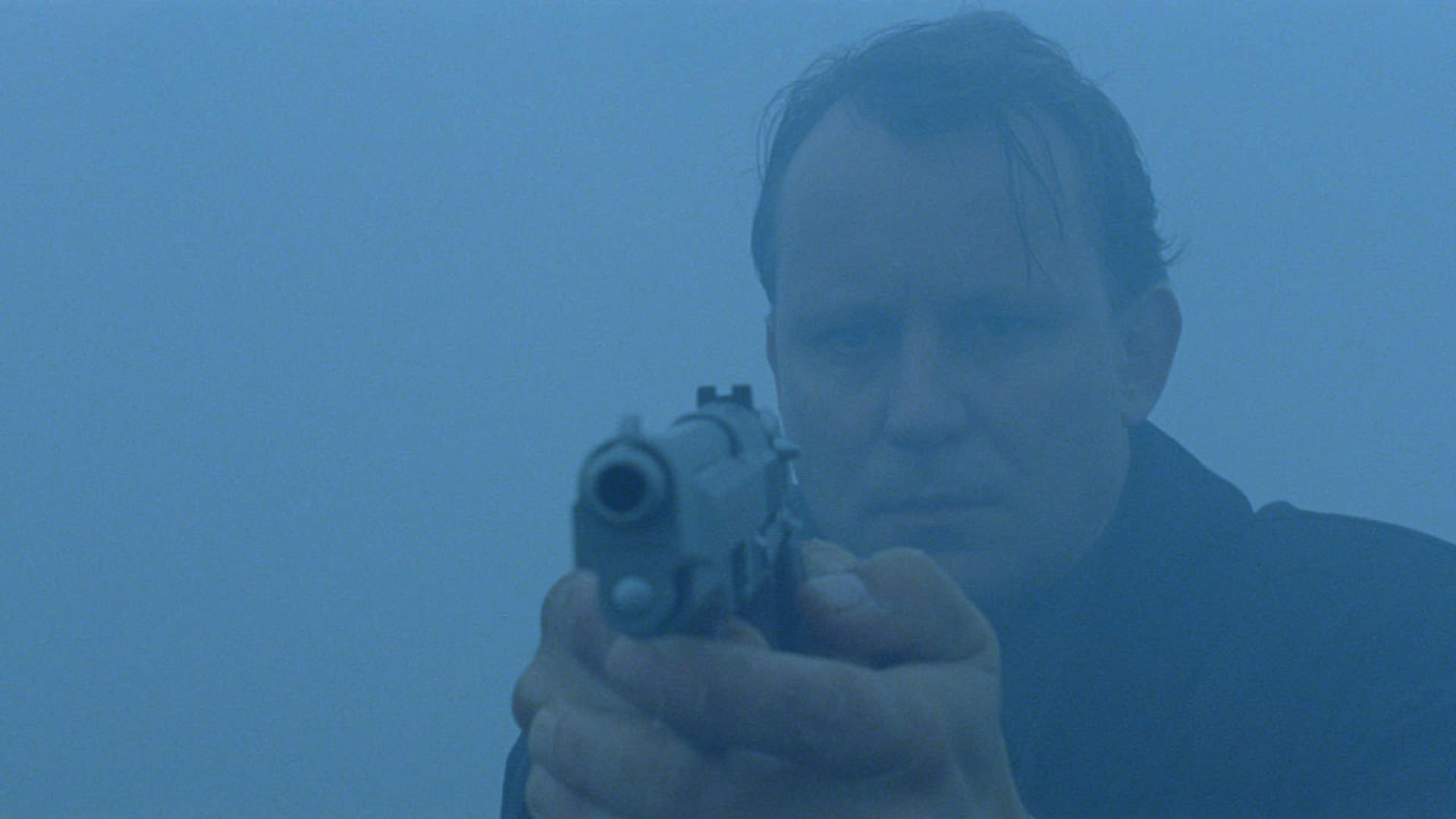 استلان اسکارسگارد در مه ایستاده با اسلحه ای به سمت او در صحنه ای از فیلم بی خوابی اریک شولدبرگ