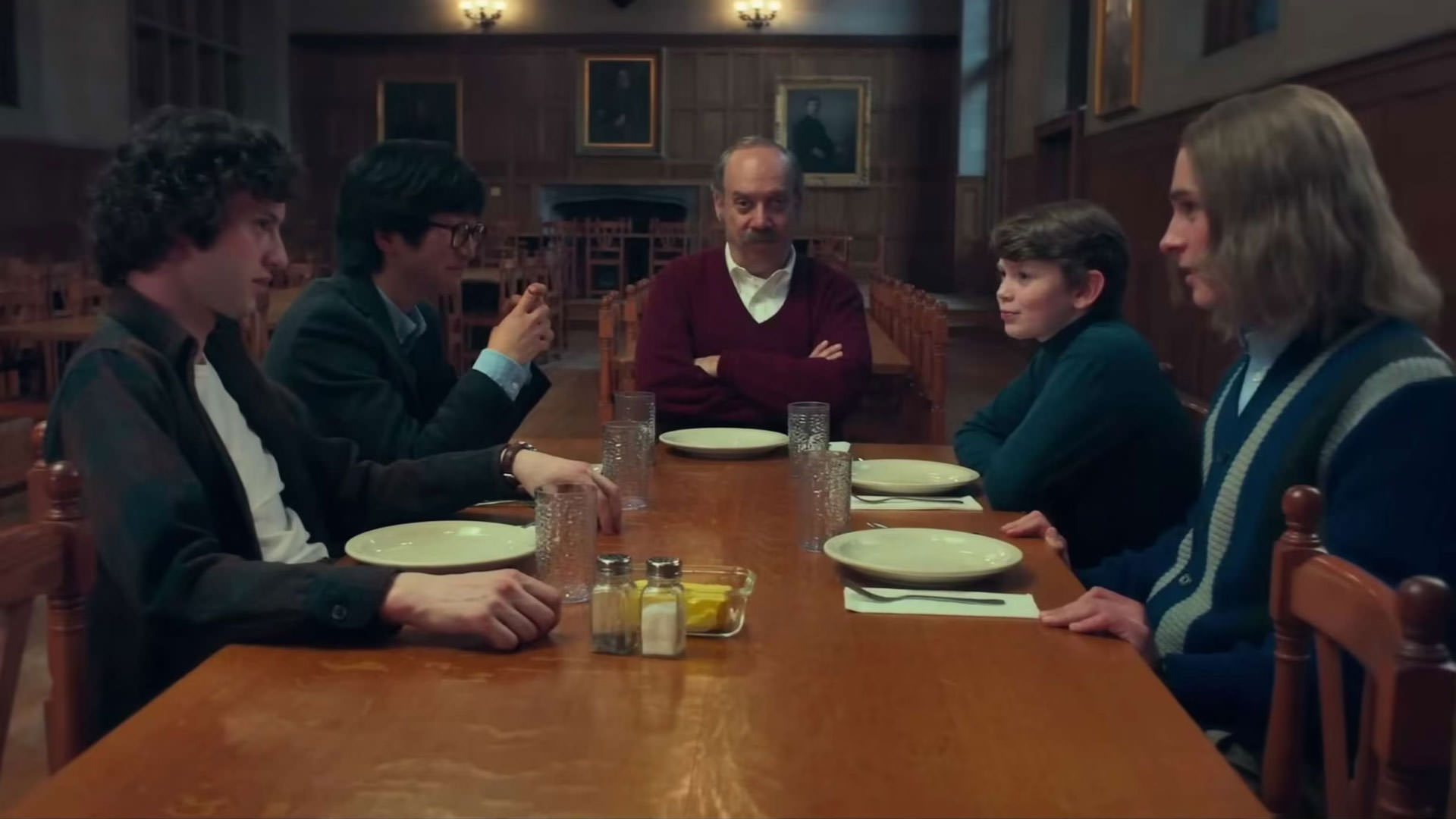 پل جیاماتی در صحنه ای از فیلم بازماندگان به کارگردانی الکساندر پین در کنار گروهی از نوجوانان روی میز مدرسه نشسته است.