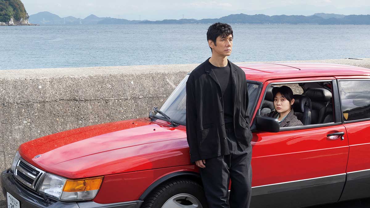 بازیگر تئاتر در کنار ماشین قرمزرنگ قدیمی با راننده حرفه ای در فیلم Drive My Car هاماگوچی