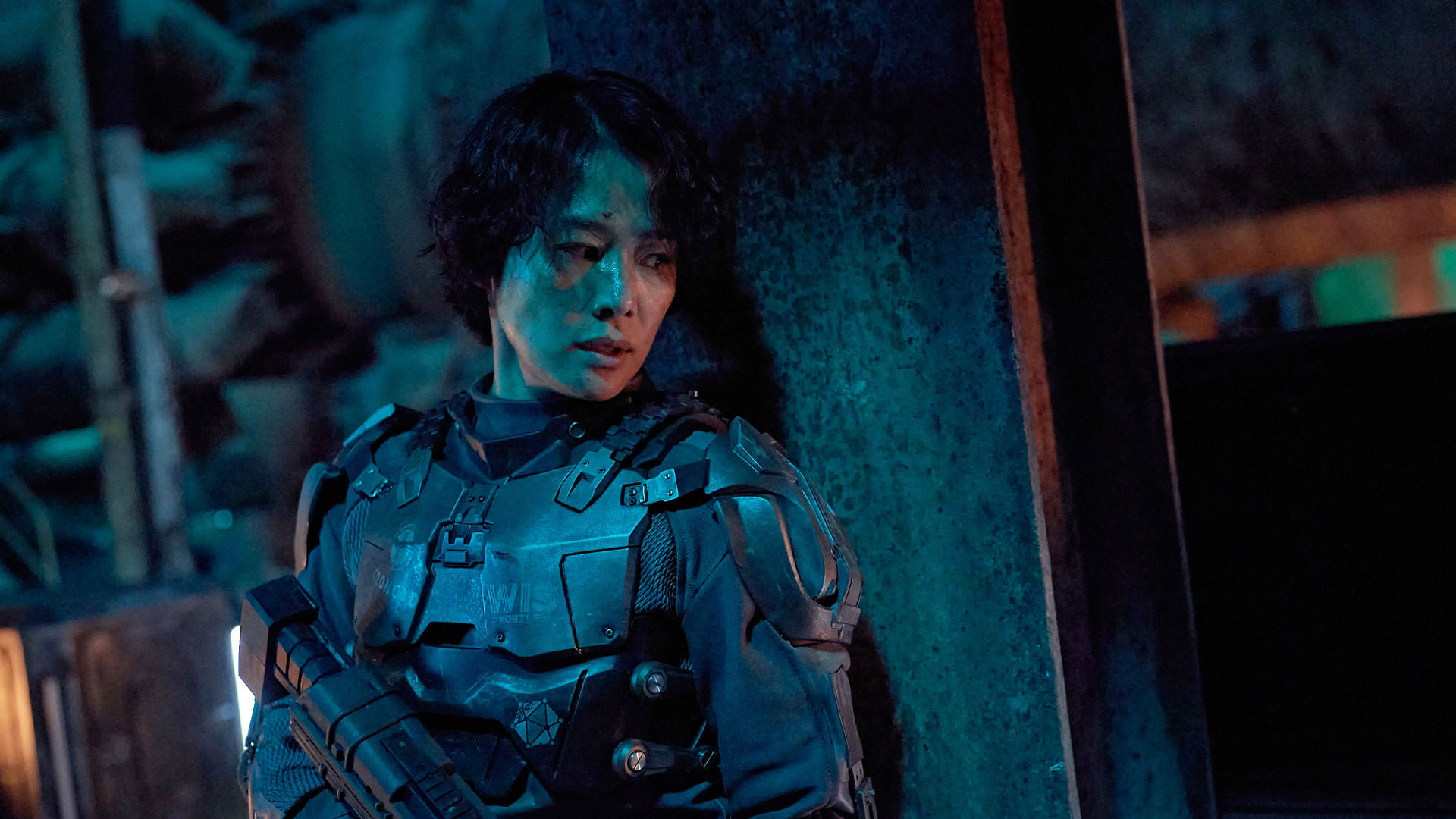 کیم هیون جو با یک لباس نظامی پیشرفته و اسلحه‌ای در دست پناه گرفته پشت یک دیوار در نمایی از فیلم جونگ ای به کارگردانی یون سانگ-هو
