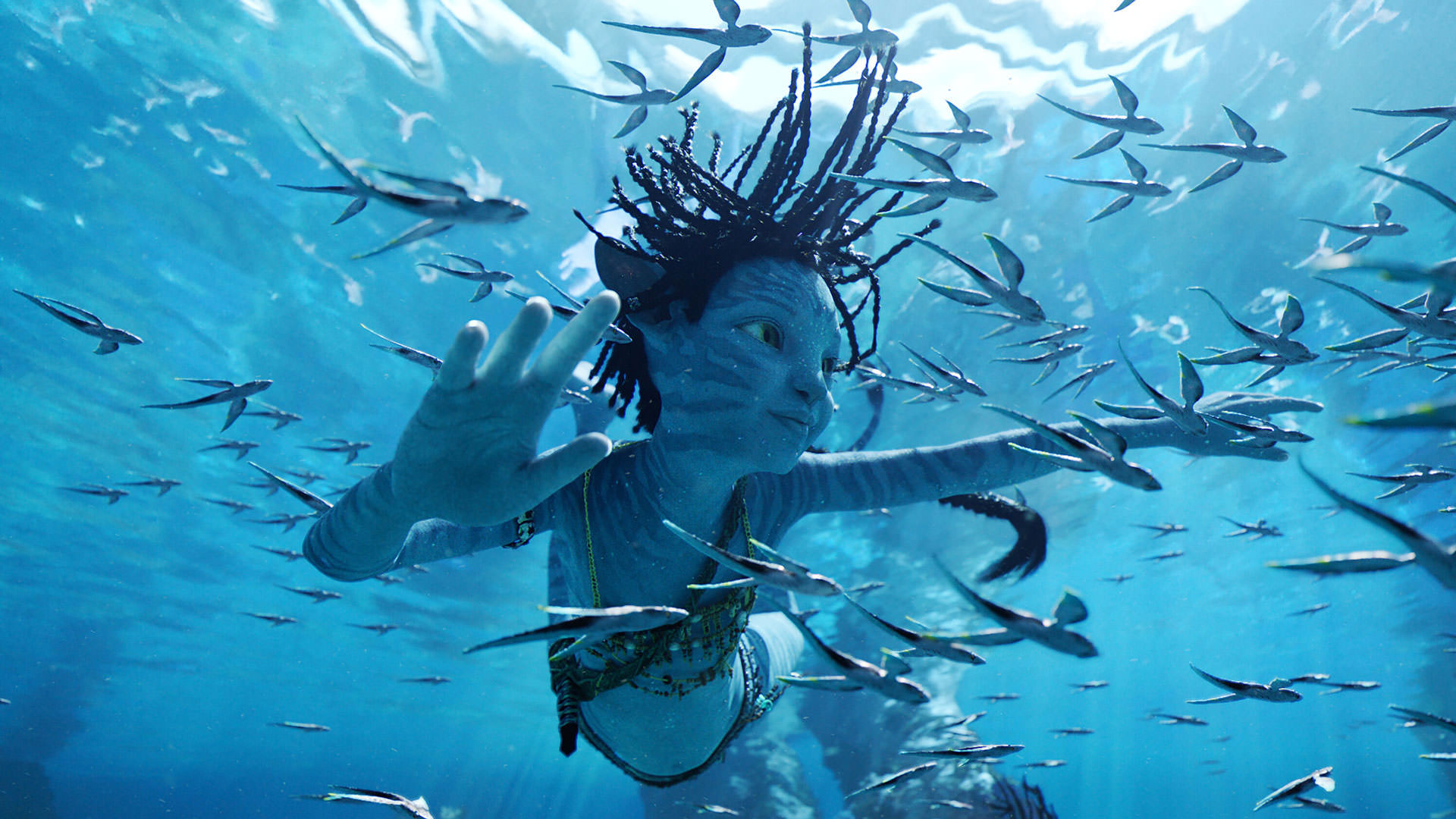 دختربچه‌ای کوچک از نژاد ناوی در حال شنا زیر آب میان ماهی‌ها در نمایی از فیلم آواتار راه آب به کارگردانی جیمز کامرون