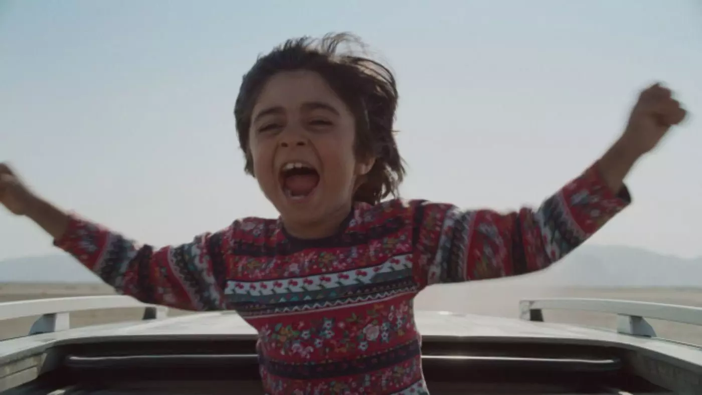 رایان سرلک ایستاده داخل سان‌روف یک ماشین در حال حرکت فریاد می‌زند در نمایی از فیلم جاده خاکی به کارگردانی پناه پناهی