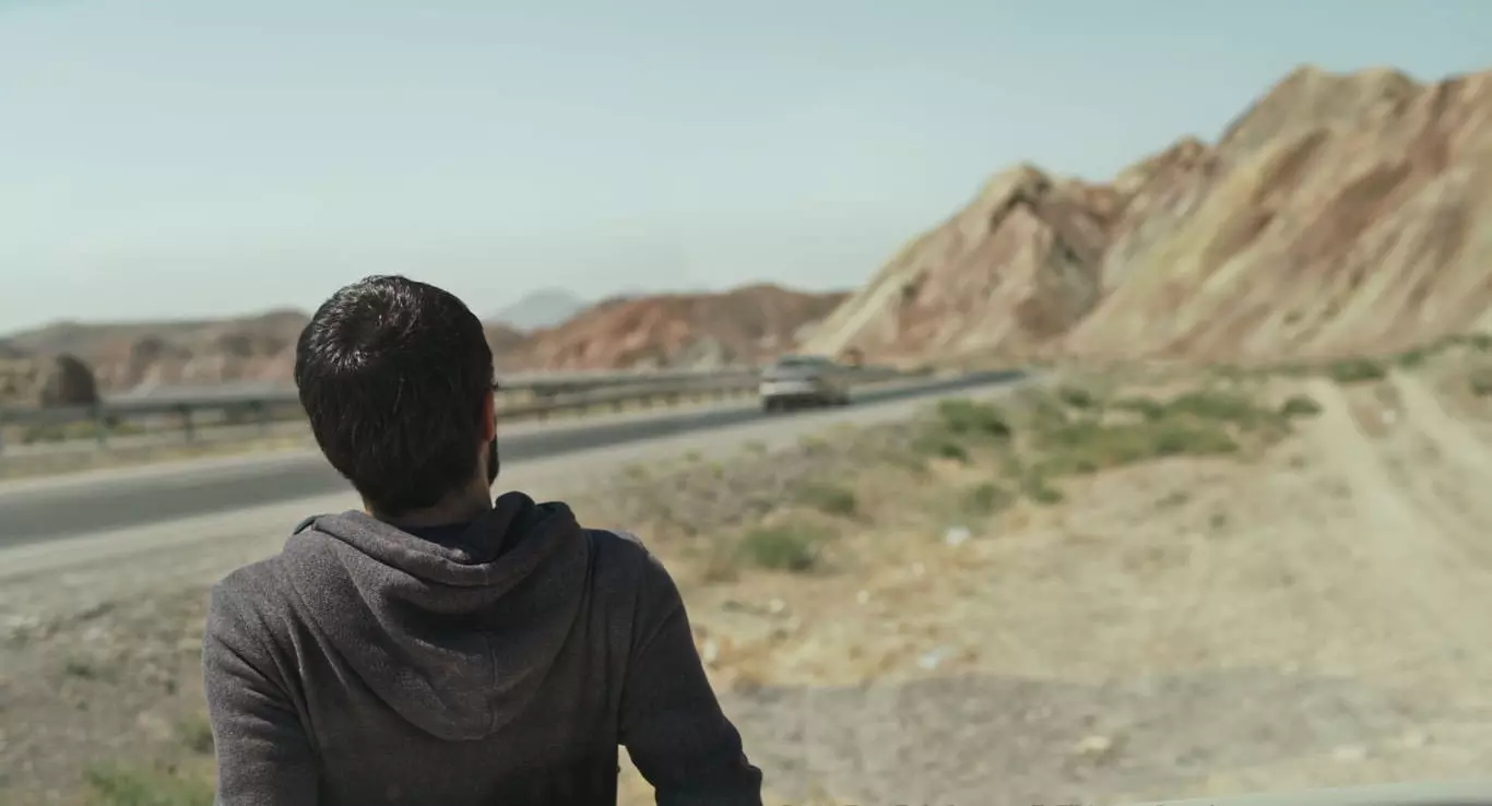 امین سیمیار در حال نگاه به جاده‌ی پیش رو در نمایی از فیلم جاده خاکی به کارگردانی پناه پناهی
