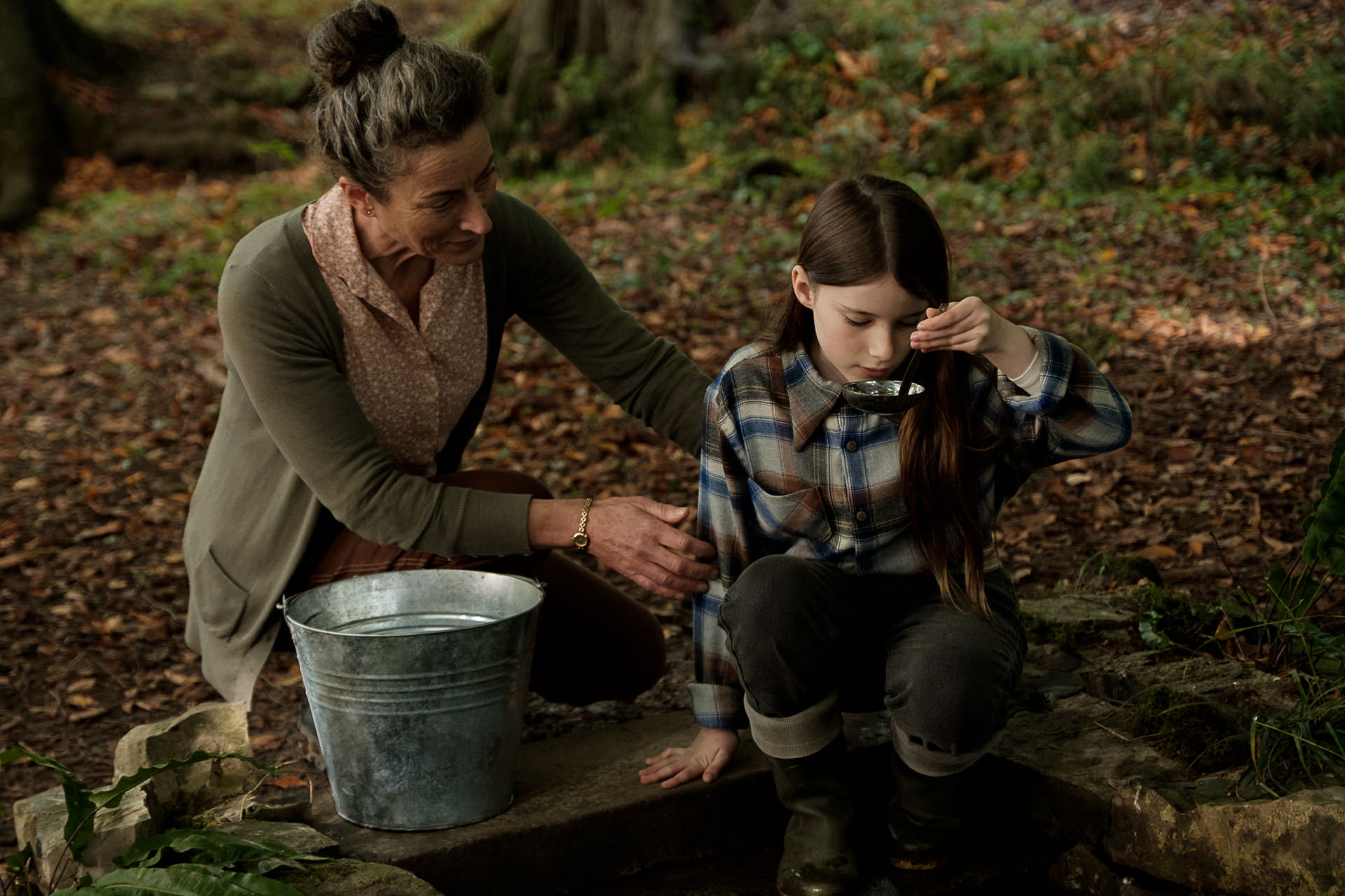 Catherine Clinch buvant de l'eau d'un puits dans la forêt à côté de Carrie Crowley dans une scène du film The Quiet Girl réalisé par Kalem Barid.