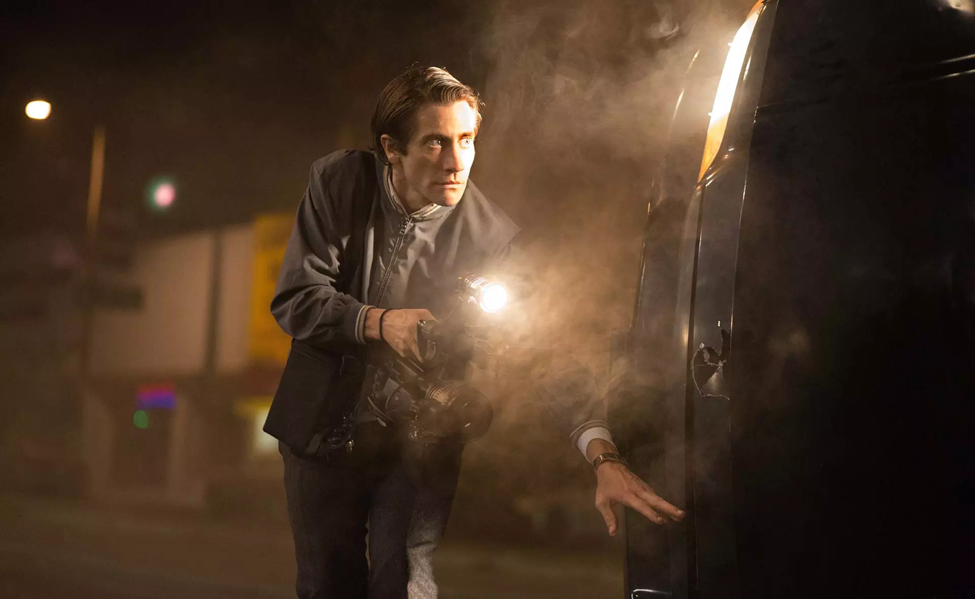 جیلنهال در فیلم شبگرد پنهان شده پشت ماشین برای گرفتن فیلم از صحنه جرم