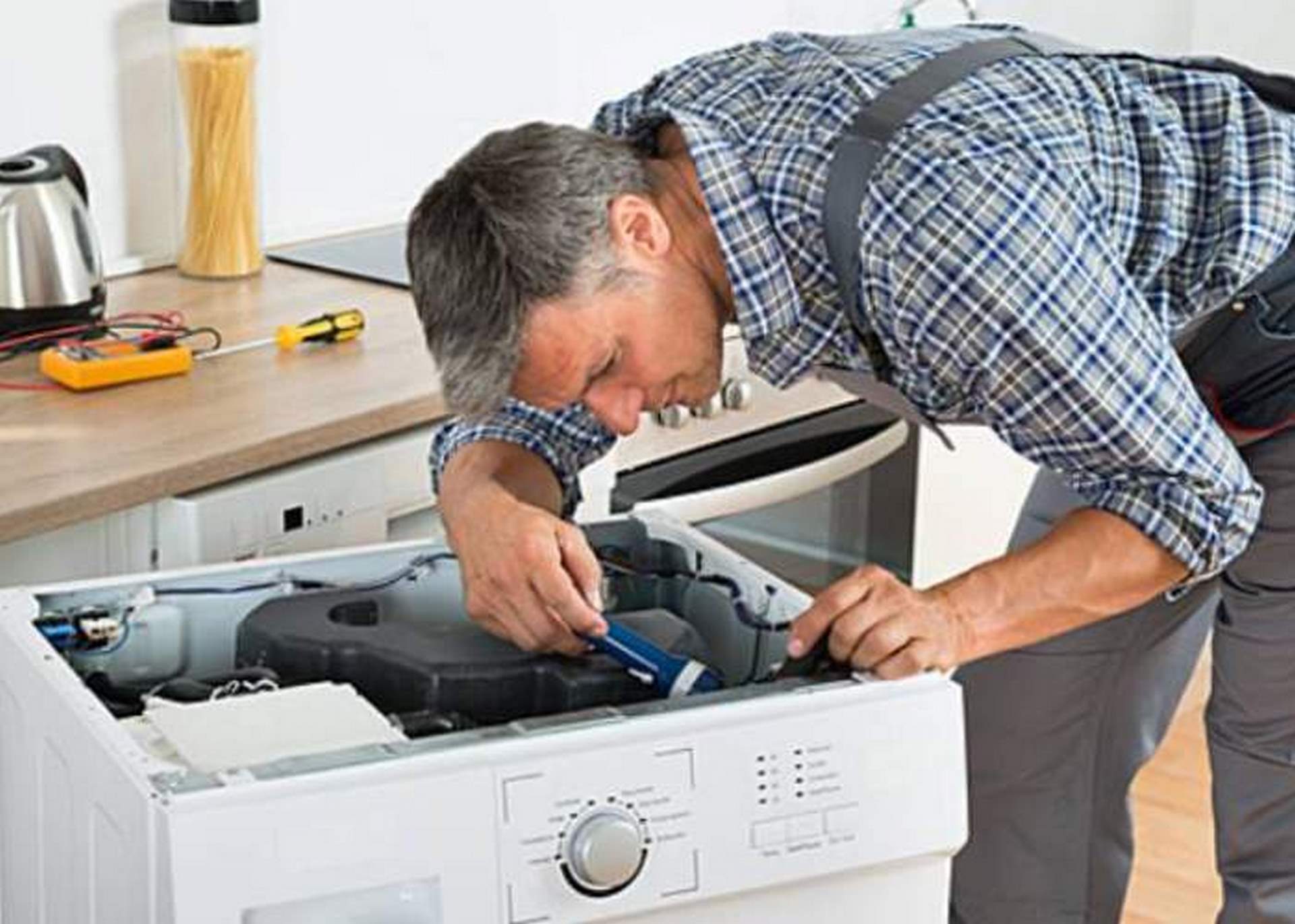 تصویر یک تعمیرکار ماشین لباس‌شویی درحال تعمیر با کمک قطعات اصلی