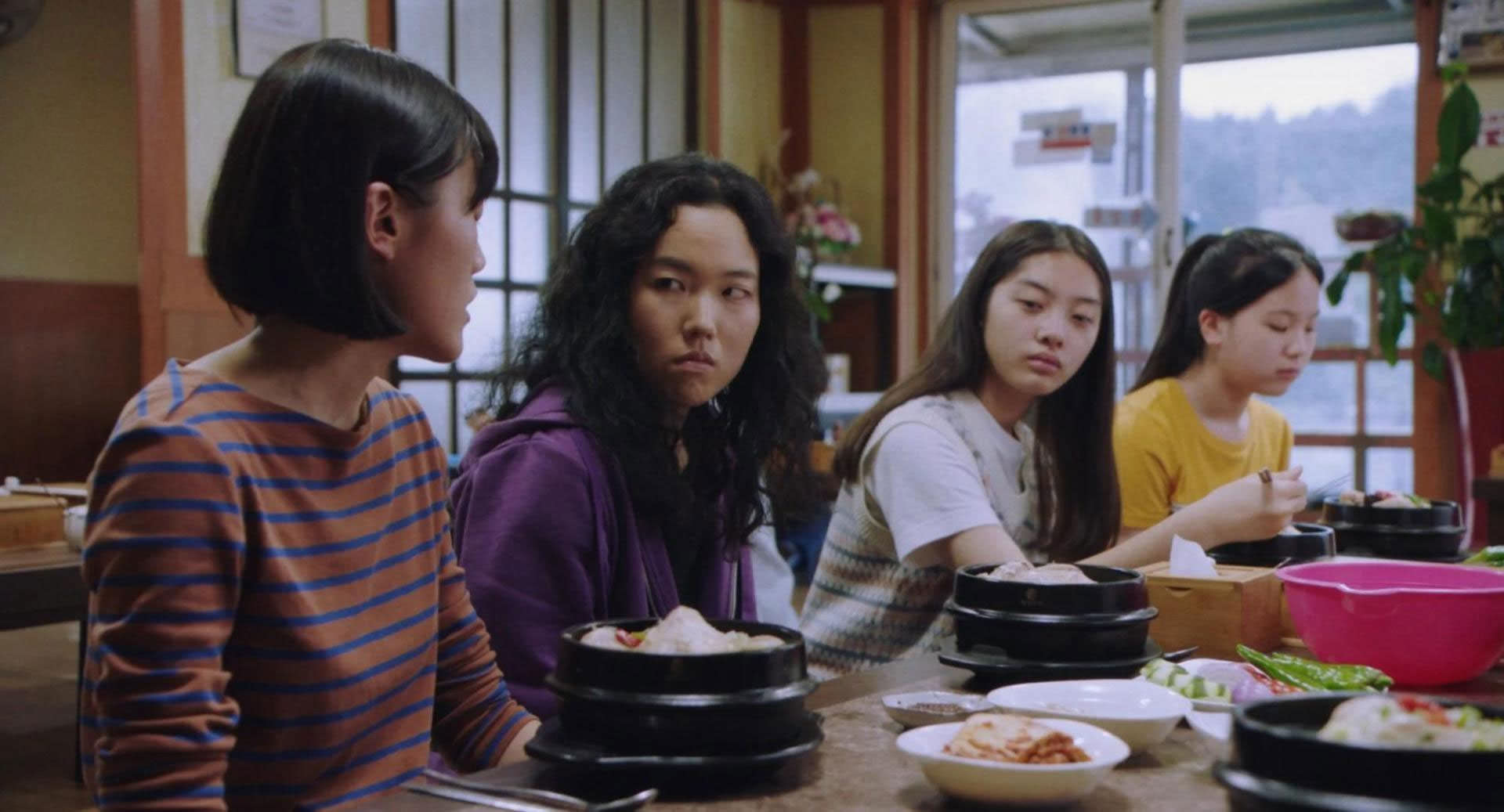 Park Ji-min parmi deux jeunes filles à une table de déjeuner à l'intérieur d'une maison traditionnelle coréenne dans une scène du film Return to Seoul réalisé par Davy Choo