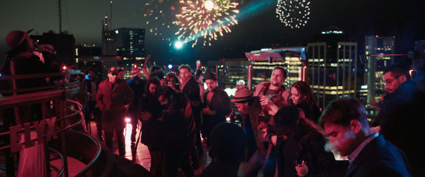 یک مهمانی شبانه در فضای باز روی پشت بام یک آپارتمان در حالی که آتش‌بازی‌هایی هم در آسمان دیده می‌شود در نمایی از فیلم برای گرفتن یک قاتل به کارگردانی دامیان شیفرون