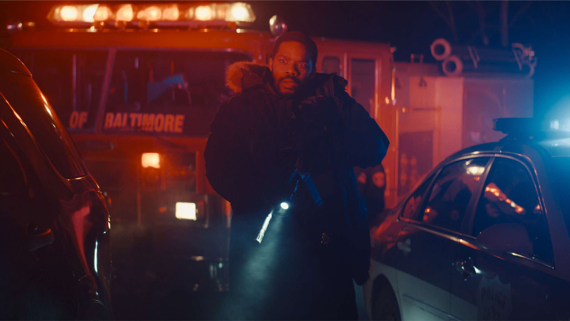 جوان آدپو با اسلحه‌ای در دست میان نور آبی و قرمز چراغ‌های ماشین‌های آتش‌نشانی و پلیس در شب در نمایی از فیلم برای گرفتن یک قاتل به کارگردانی دامیان شیفرون