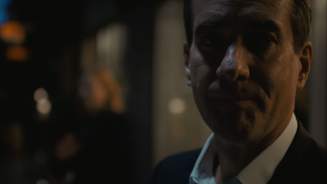 متیو مک‌فدین رو بالکن یک آپارتمان در شب در حالی که سارا اسنوک پشت سرش به شکل محوی دیده می‌شود در نمایی از سریال وراثت