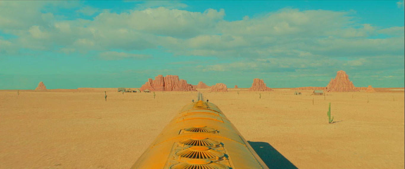قطاری زرد رنگ در حال عبور از میان بیابان در نمایی از فیلم استروید سیتی به کارگردانی وس اندرسون