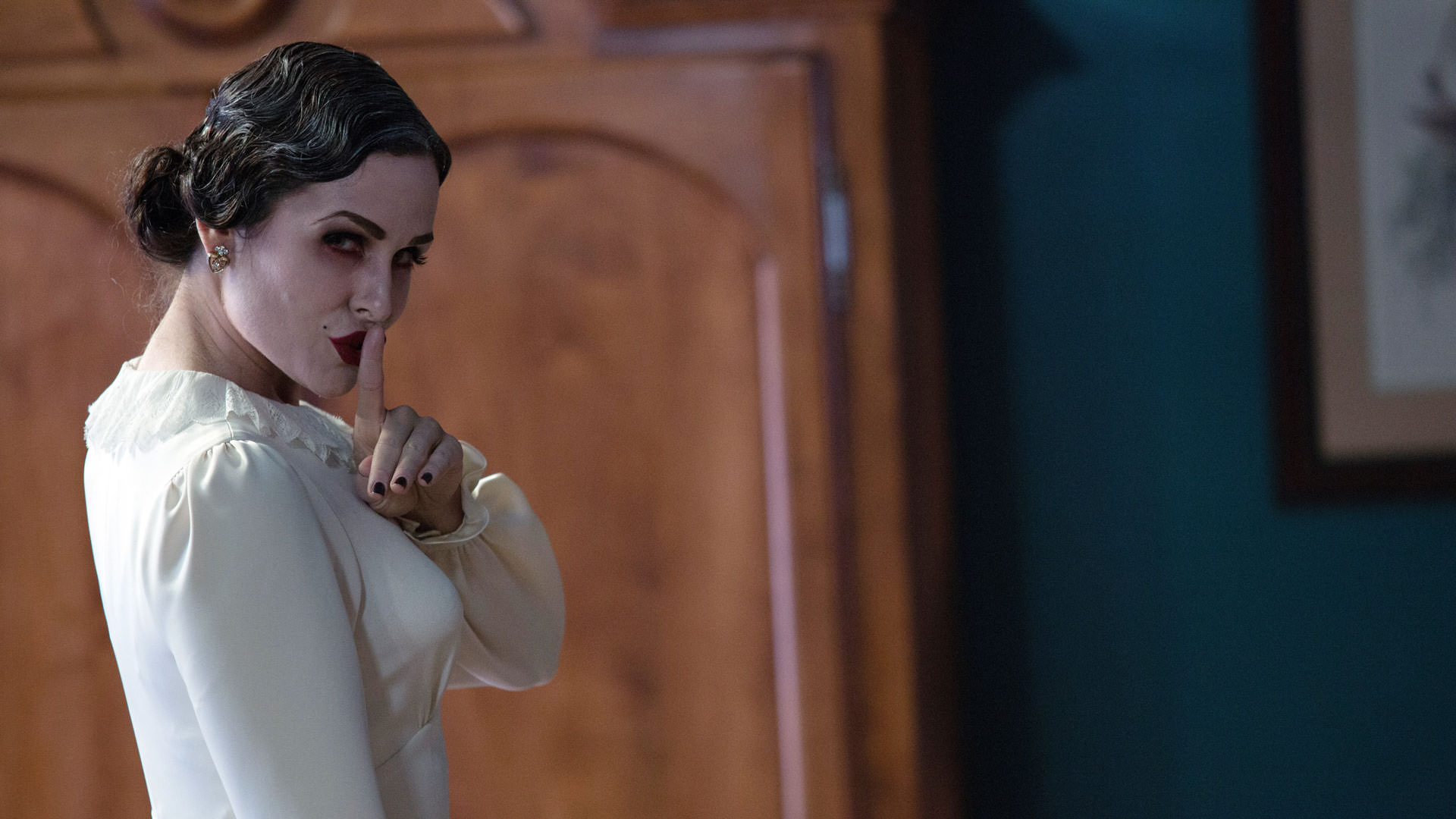 یک زن سفیدپوش در هال نشان دادن علامت هیس در نمایی از فیلم توطئه‌آمیز: قسمت دوم به کارگردانی جیمز وان