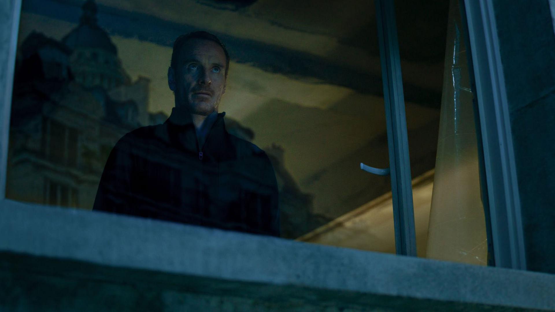 مایکل فاسبندر در نقش آدمکش در حال تماشا از پنجره در فیلم The Killer 