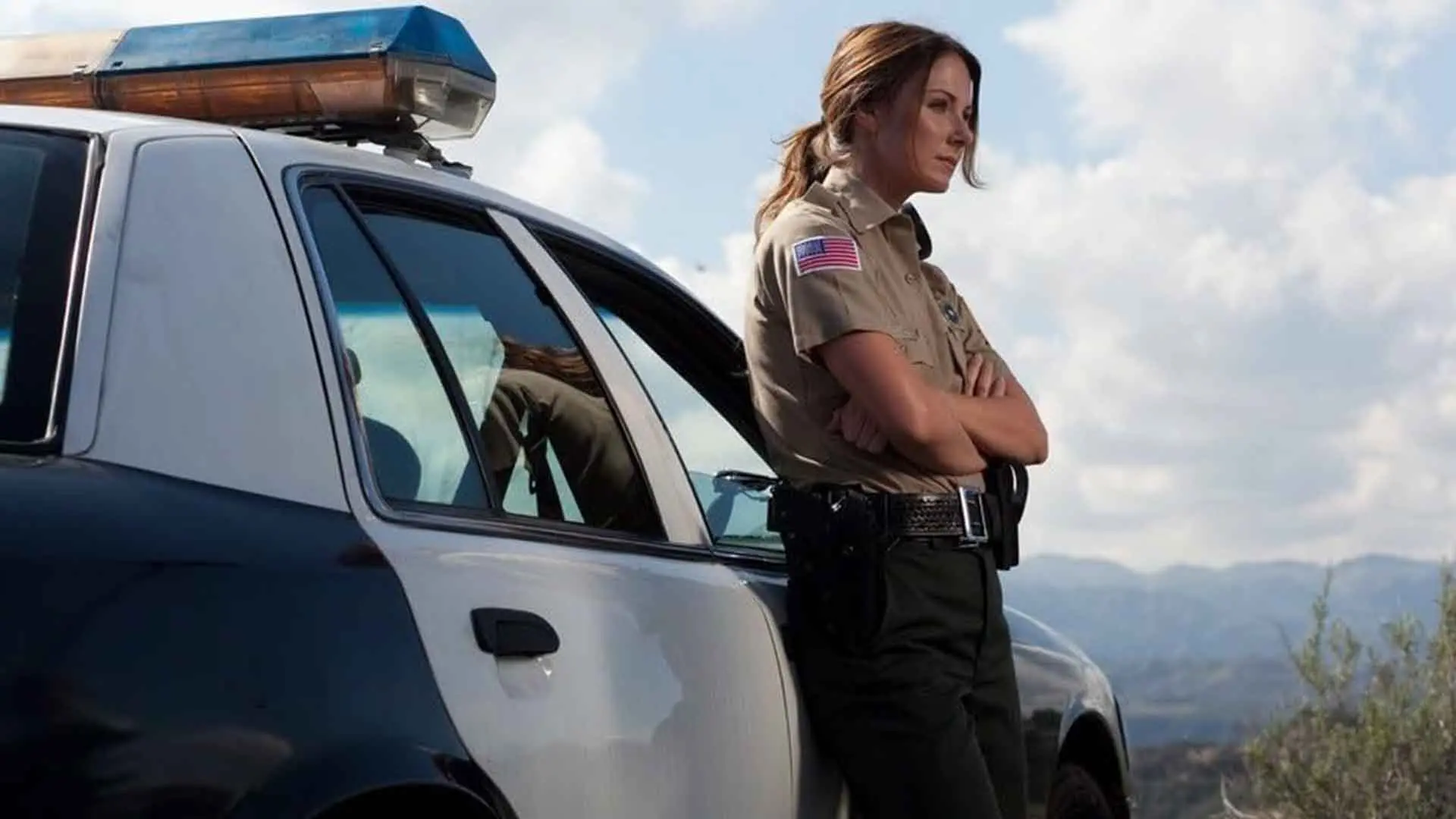 یک پلیس زن در فیلم Sand Sharks به ماشین پلیس تکیه داده است